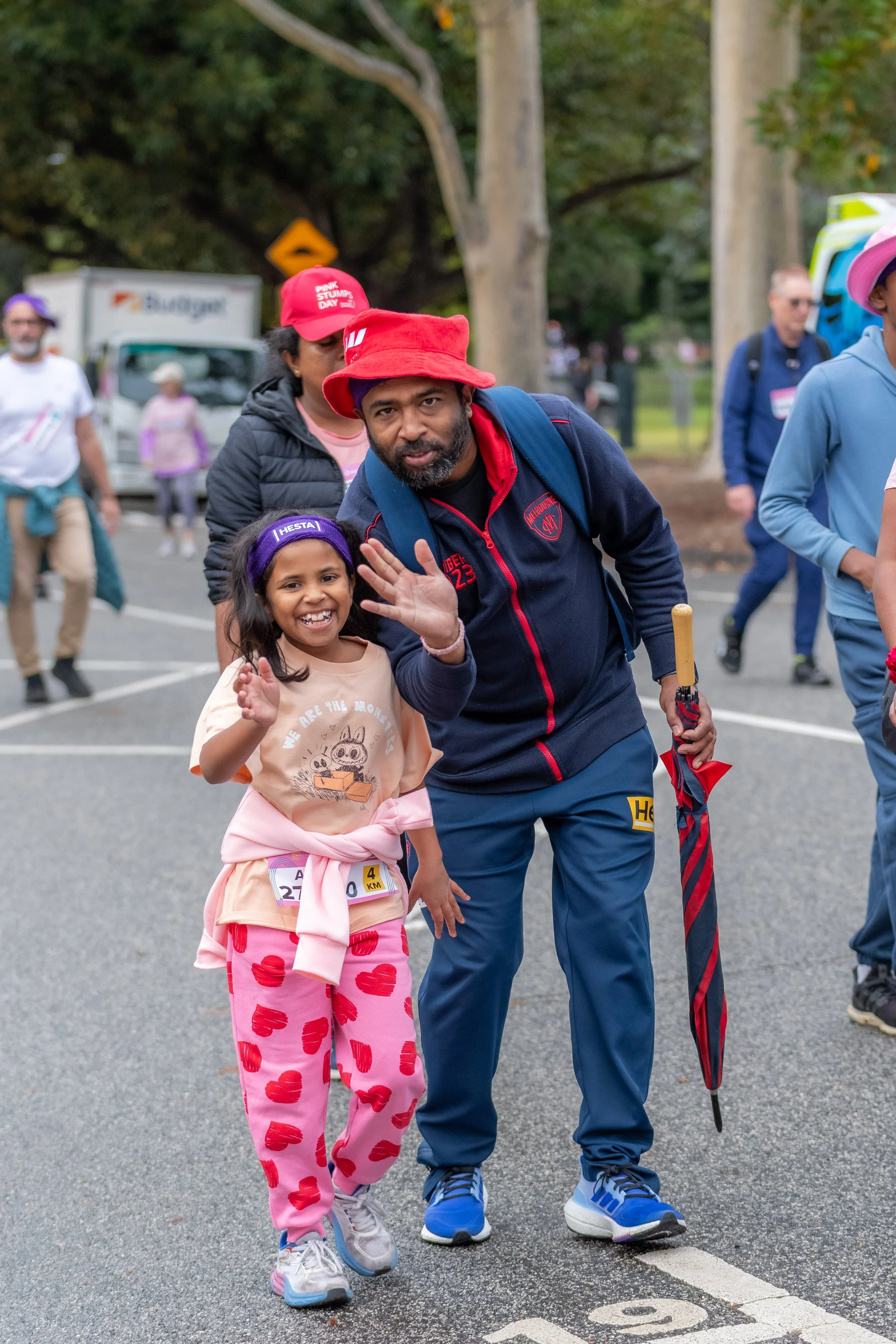 An adult racegoer bends down towards a child and they both smile and wave at the camera.