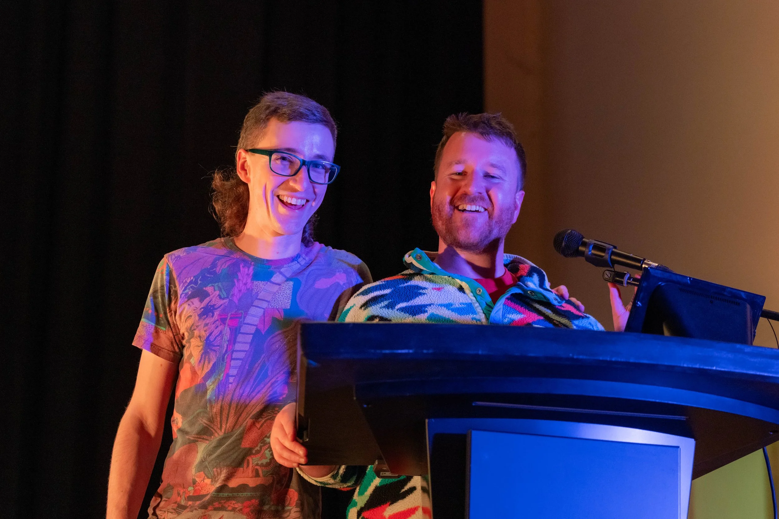 Two humans stand behind a podium and smile at the camera.