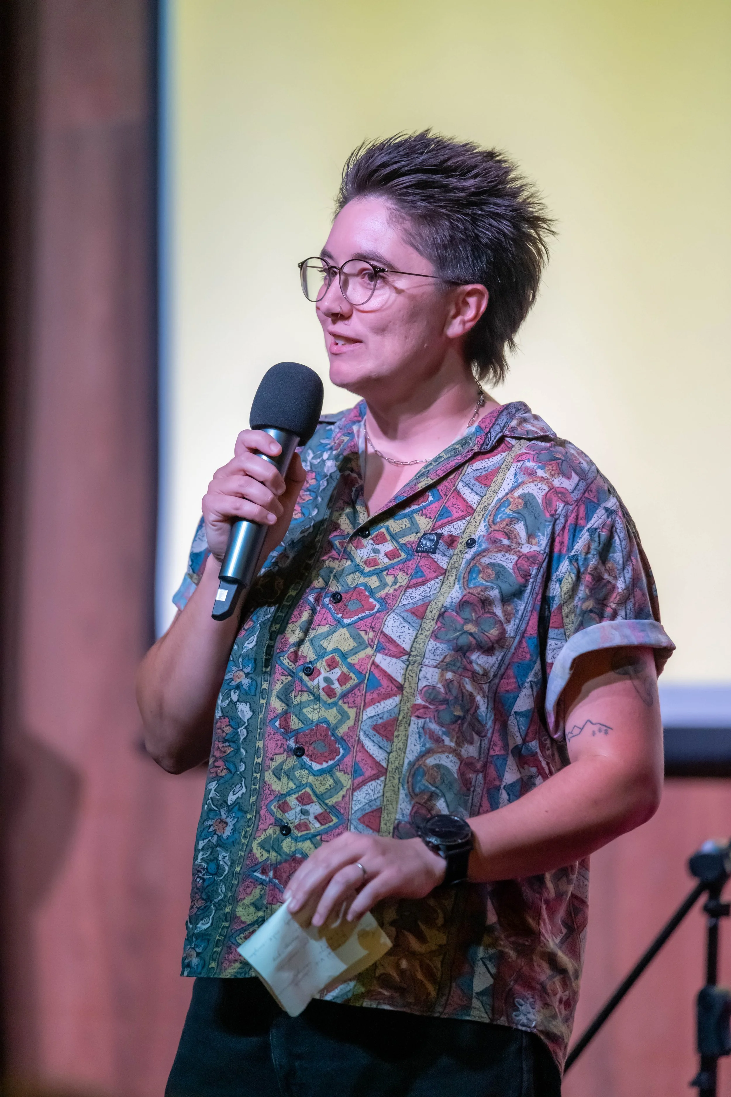 A human with short brown hair speaks into a microphone.