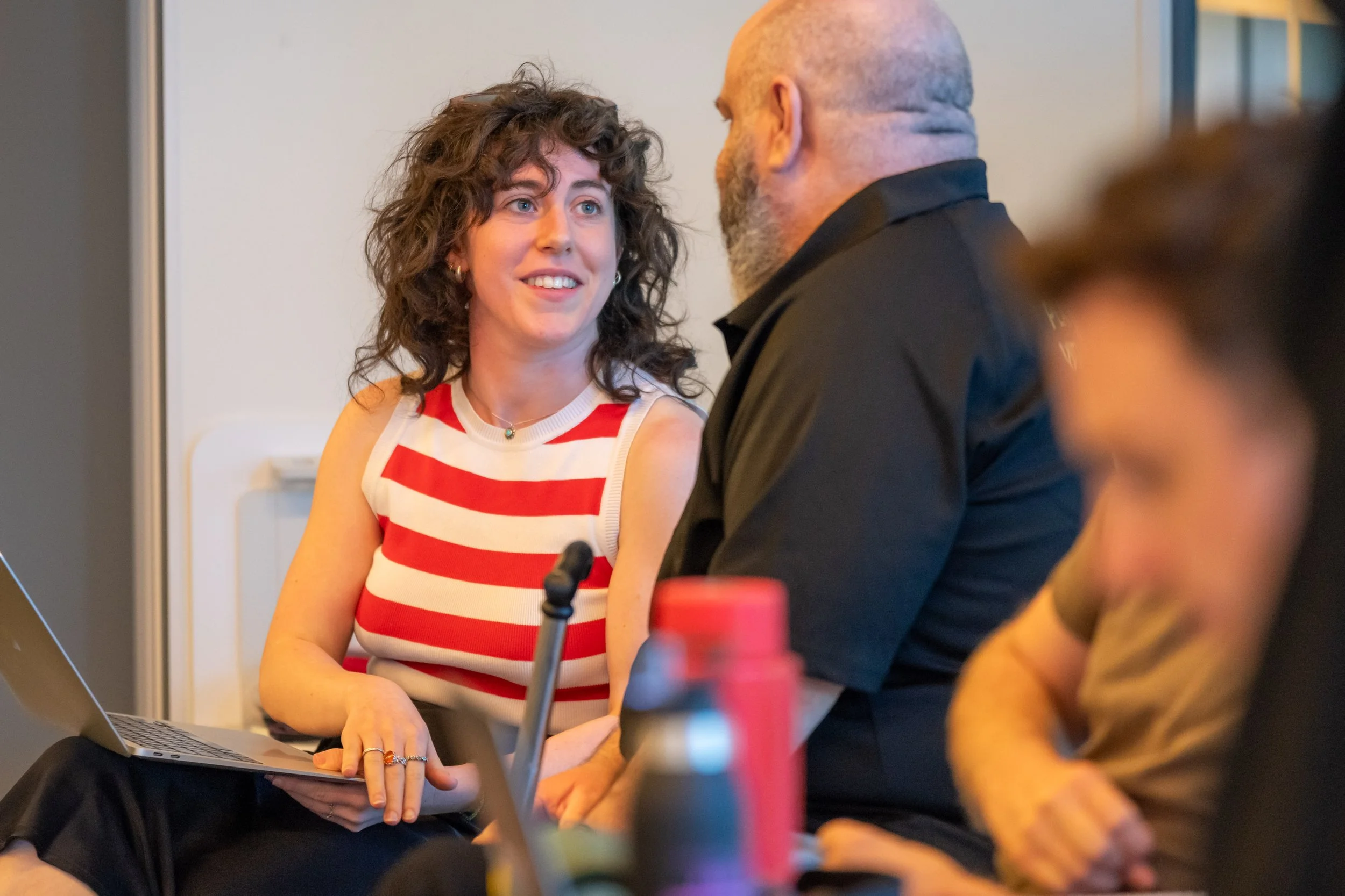 Two humans sit in conversation. One has a laptop on their lap.