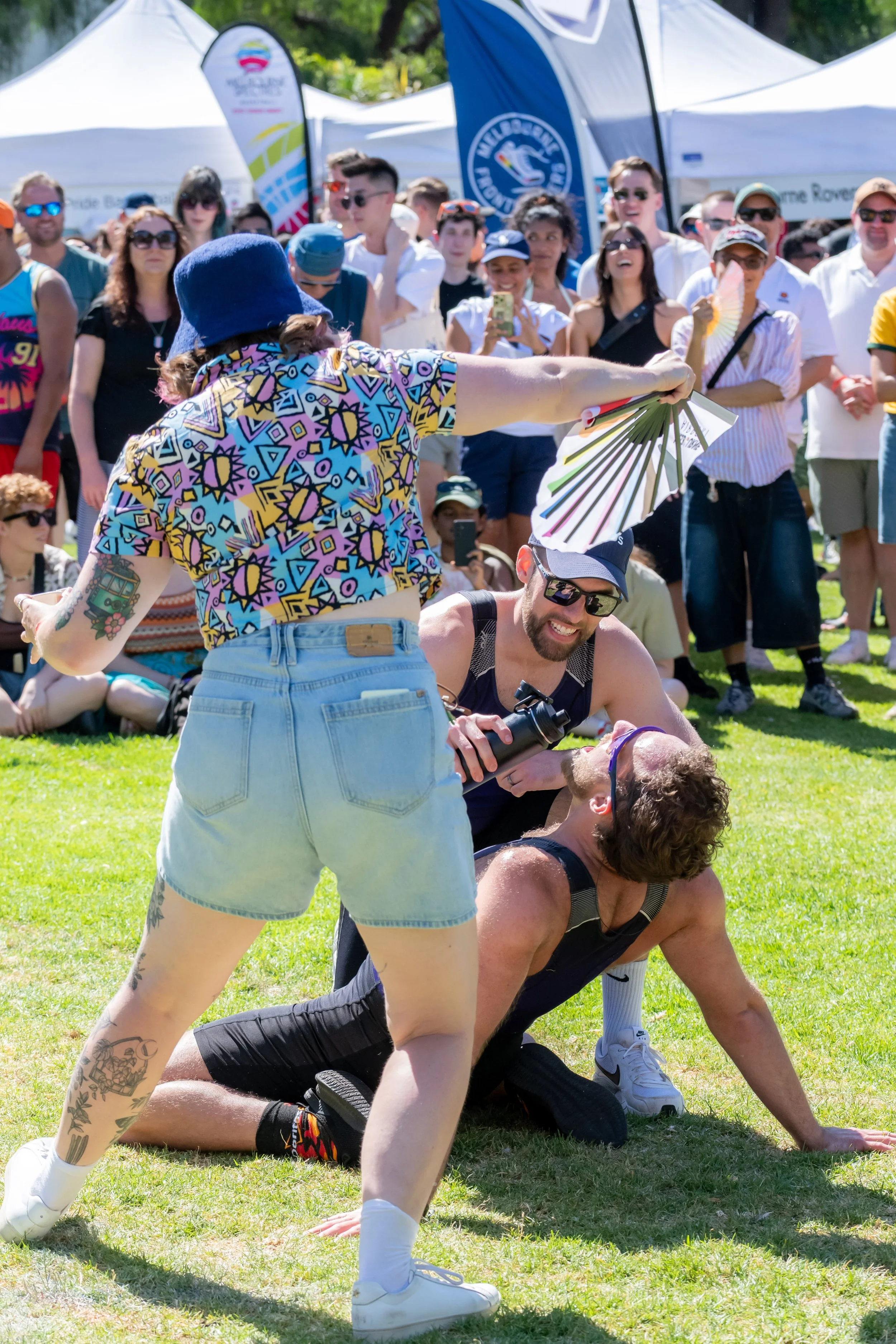 A human is beiing fanned by another human standing over them, whilst being refreshed with water by their teammate.