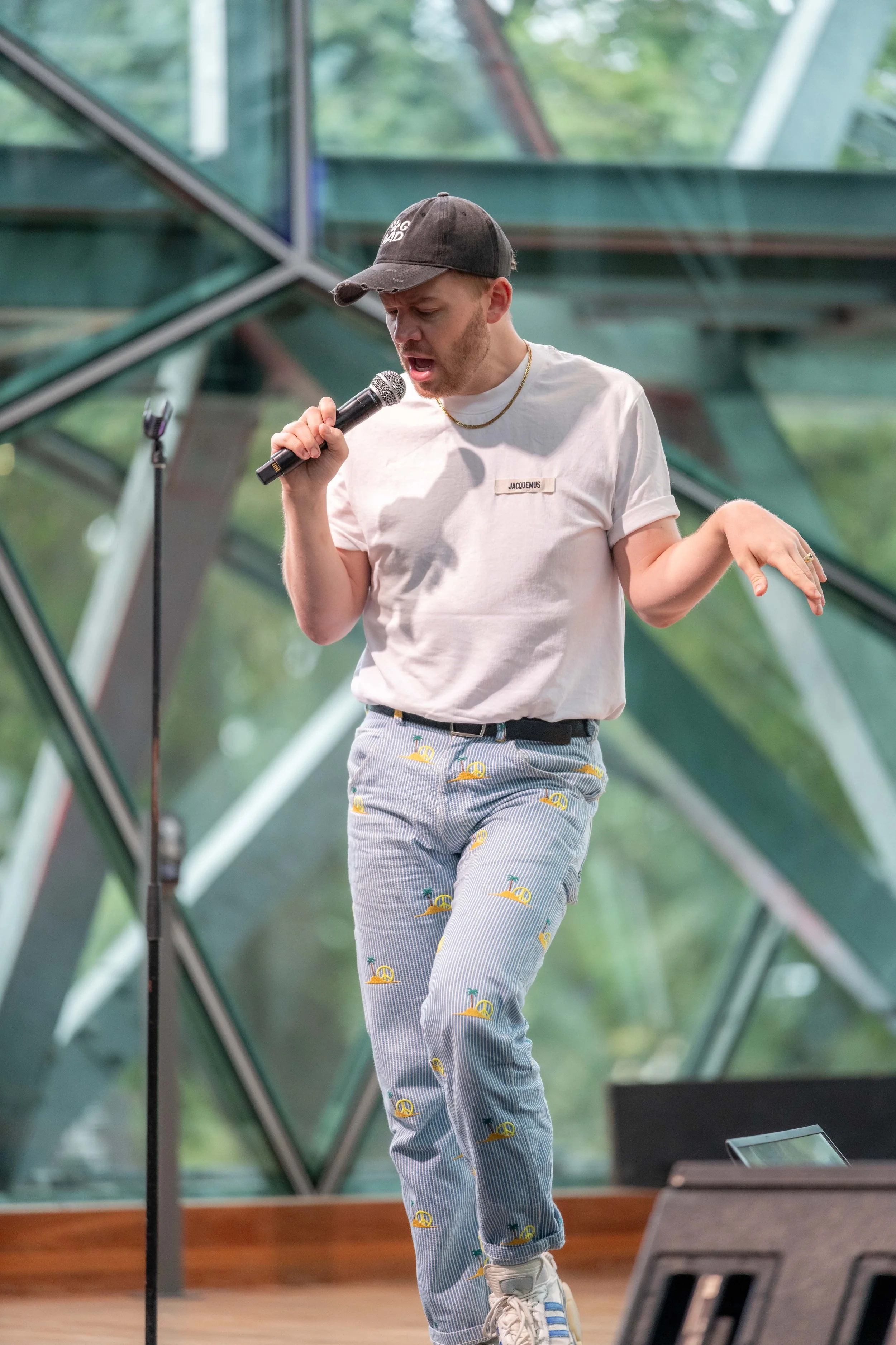 Joel Creasey stands, with a limp hand out, whilst speaking into a microphone.