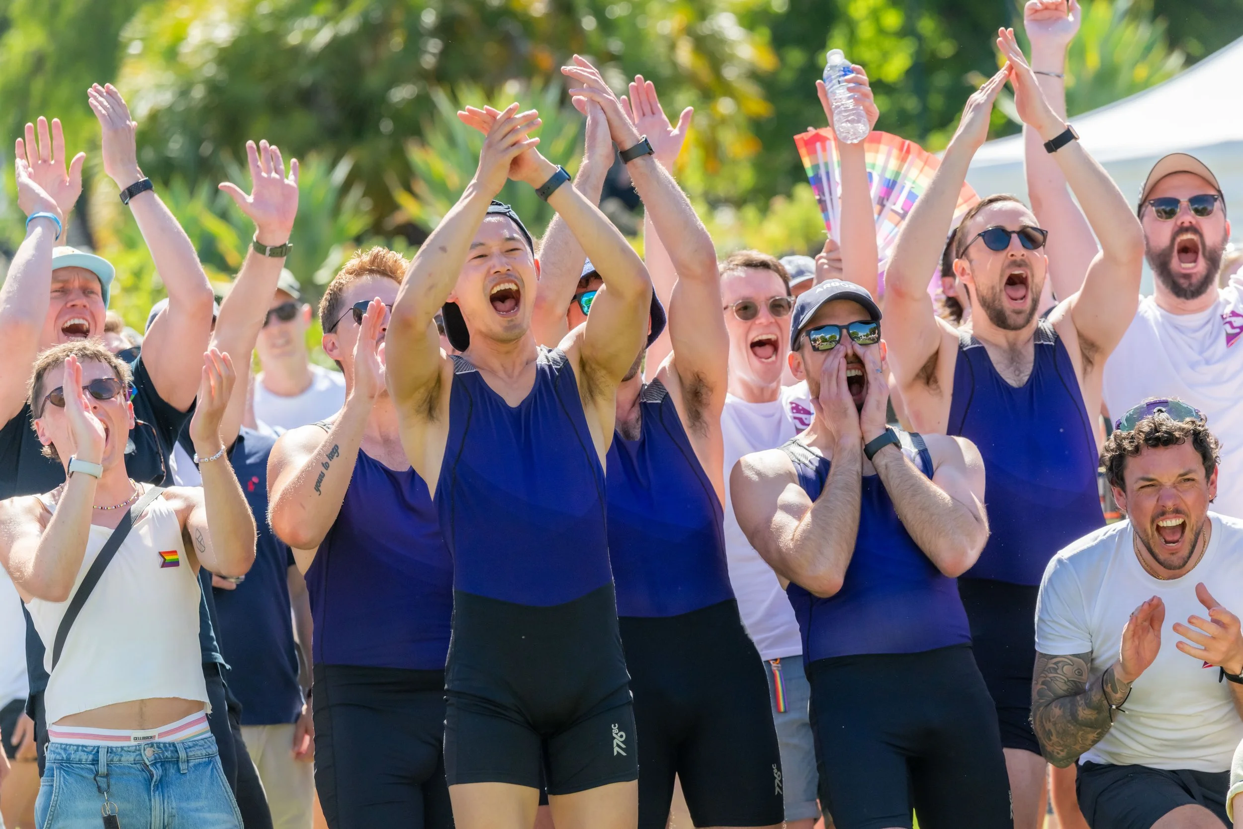 Humans wearing blue and black lycra outfits raise their arms in the air as they cheer.