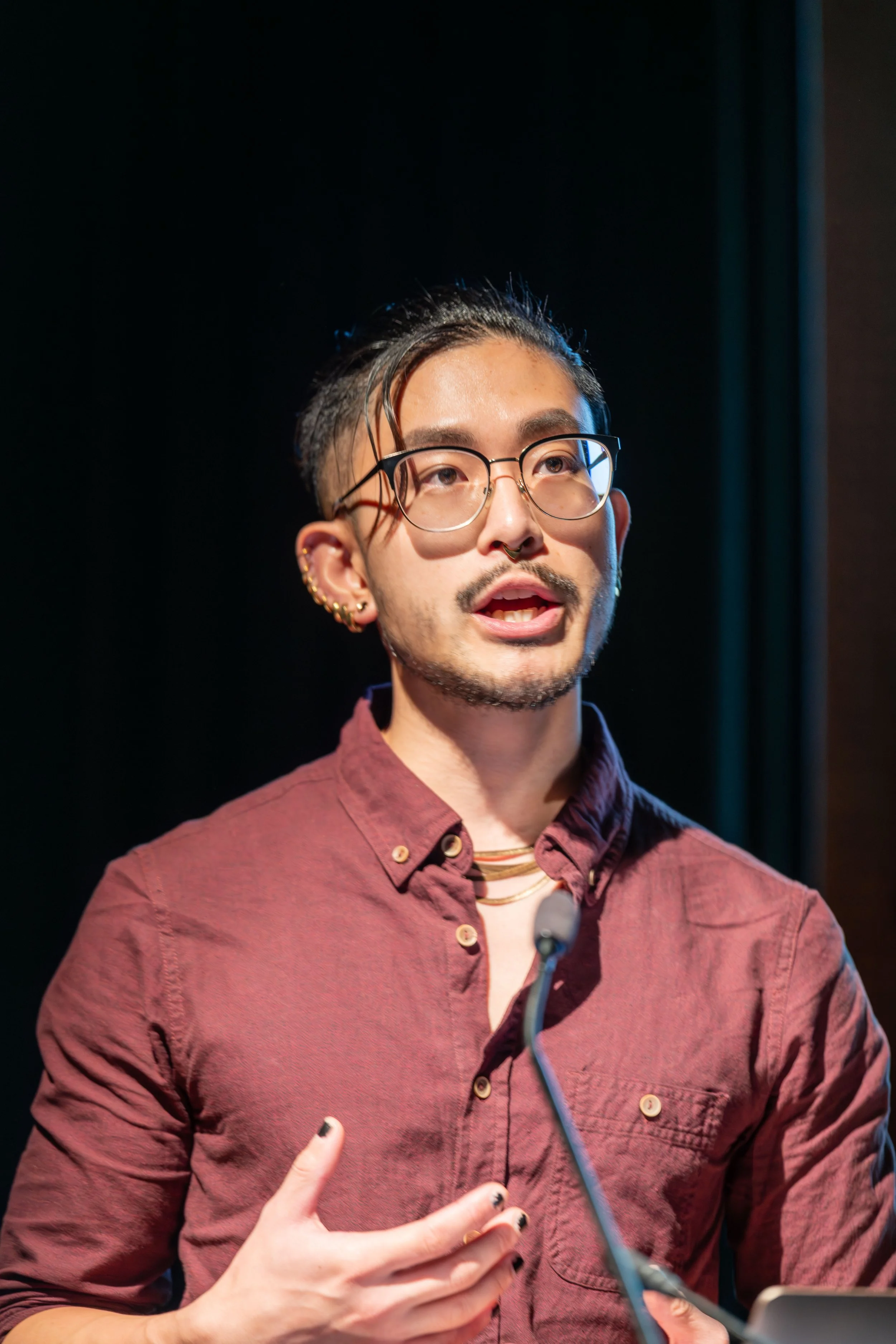 A human speaks into the microphone whilst looking at an unseen audience.