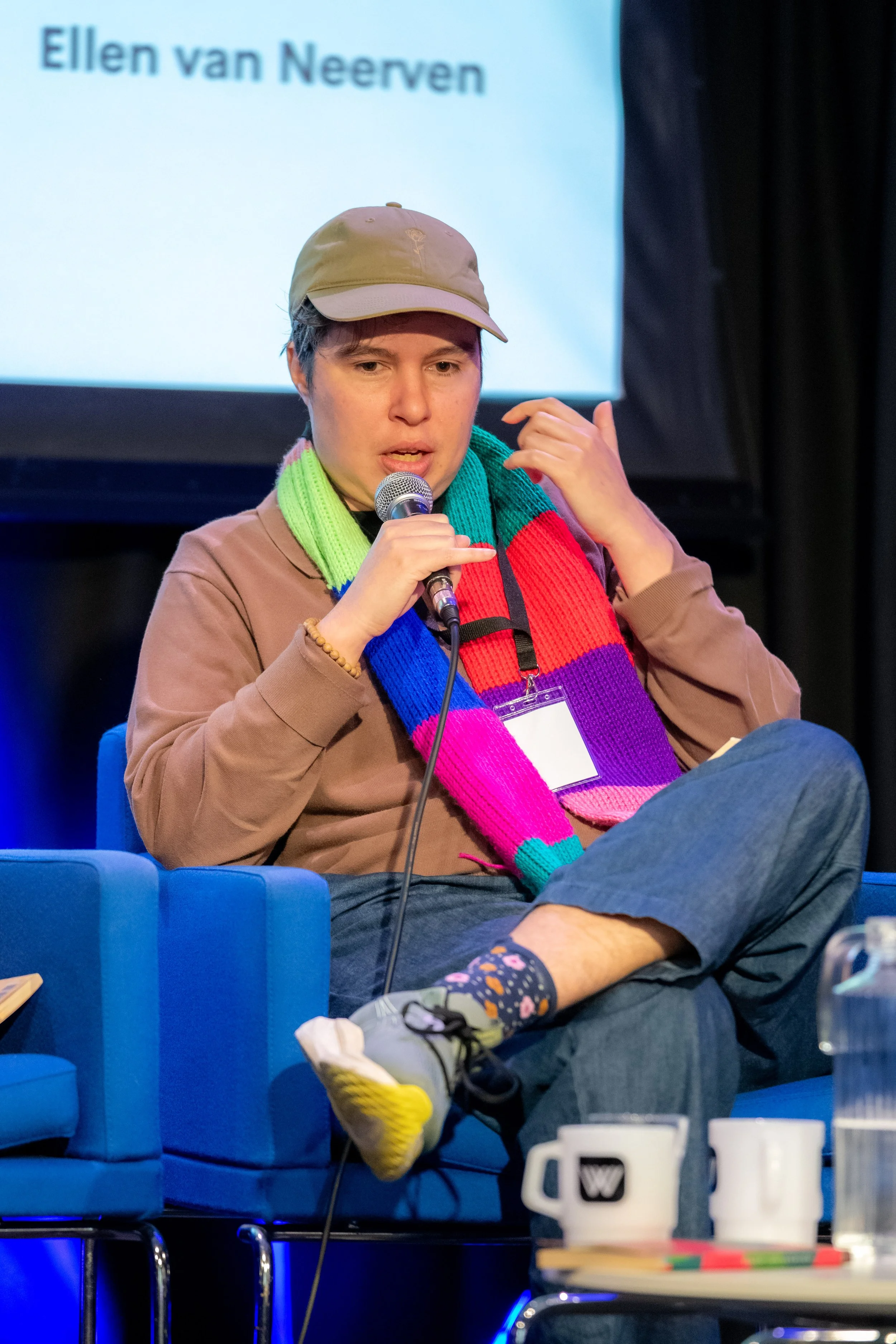 A panelist wearing a scarf speaks into a microphone.