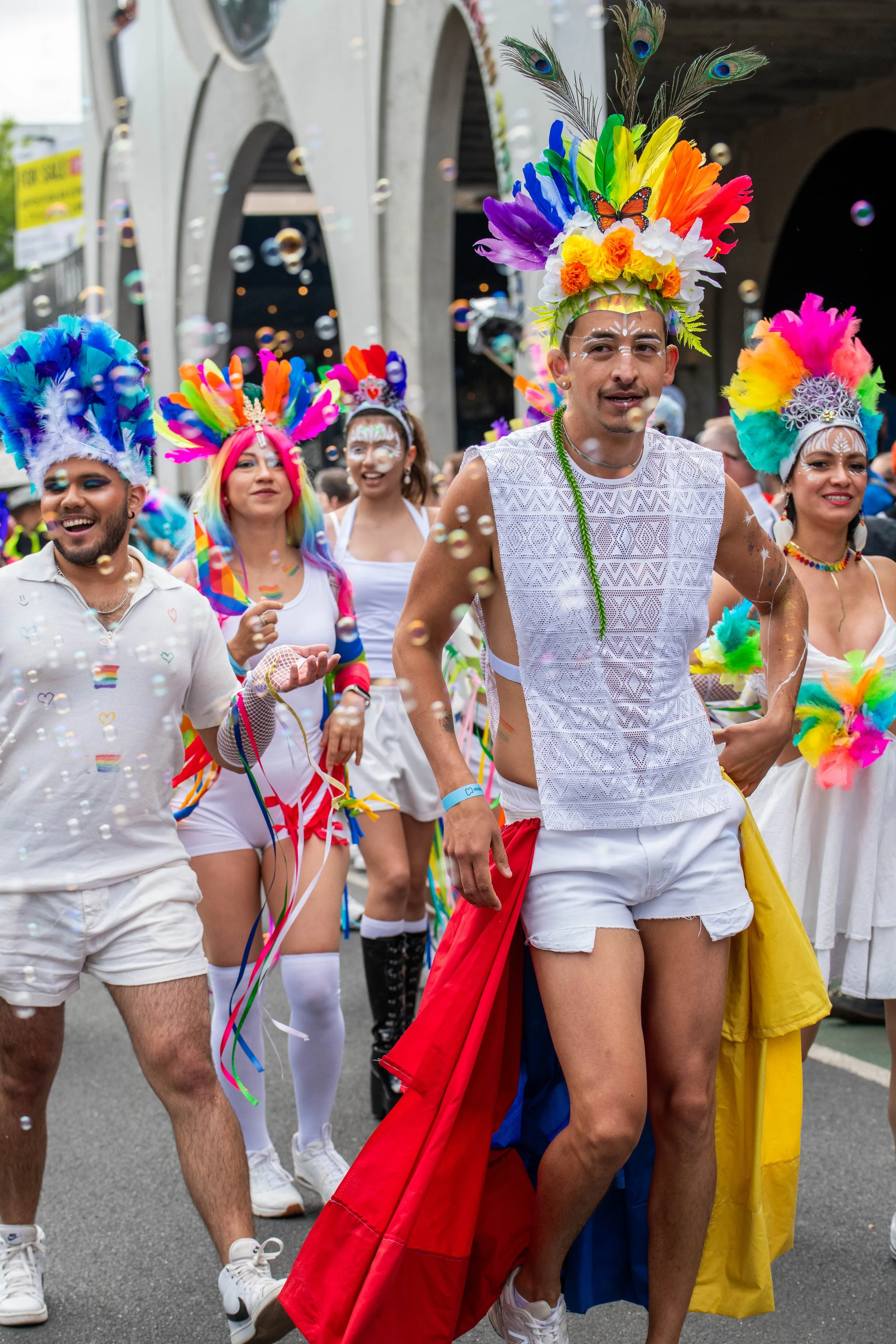 Humans in white and colourful headresses dance amongst bubbles.