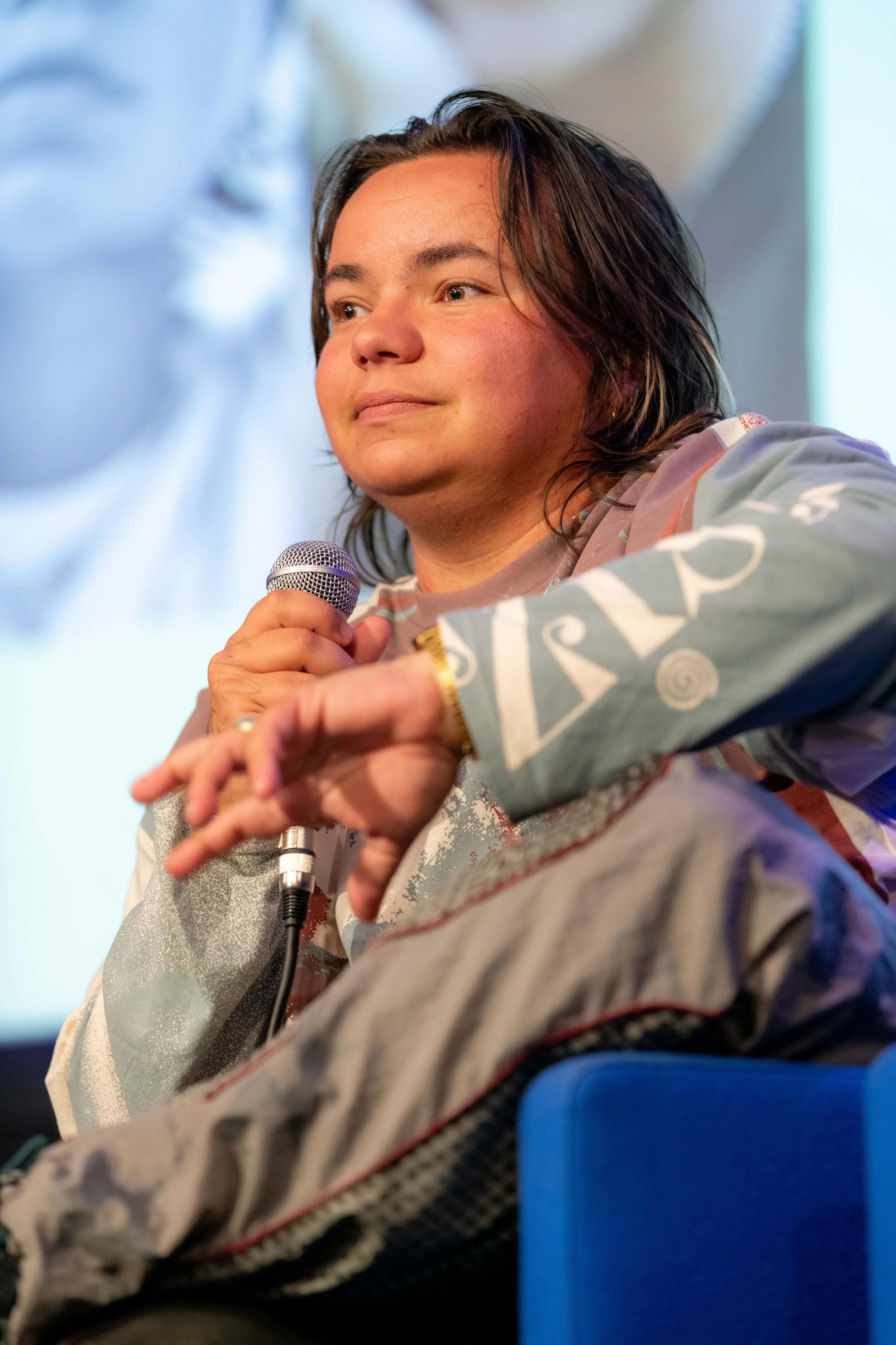 A panelist with brown hair speaks into a microphone.