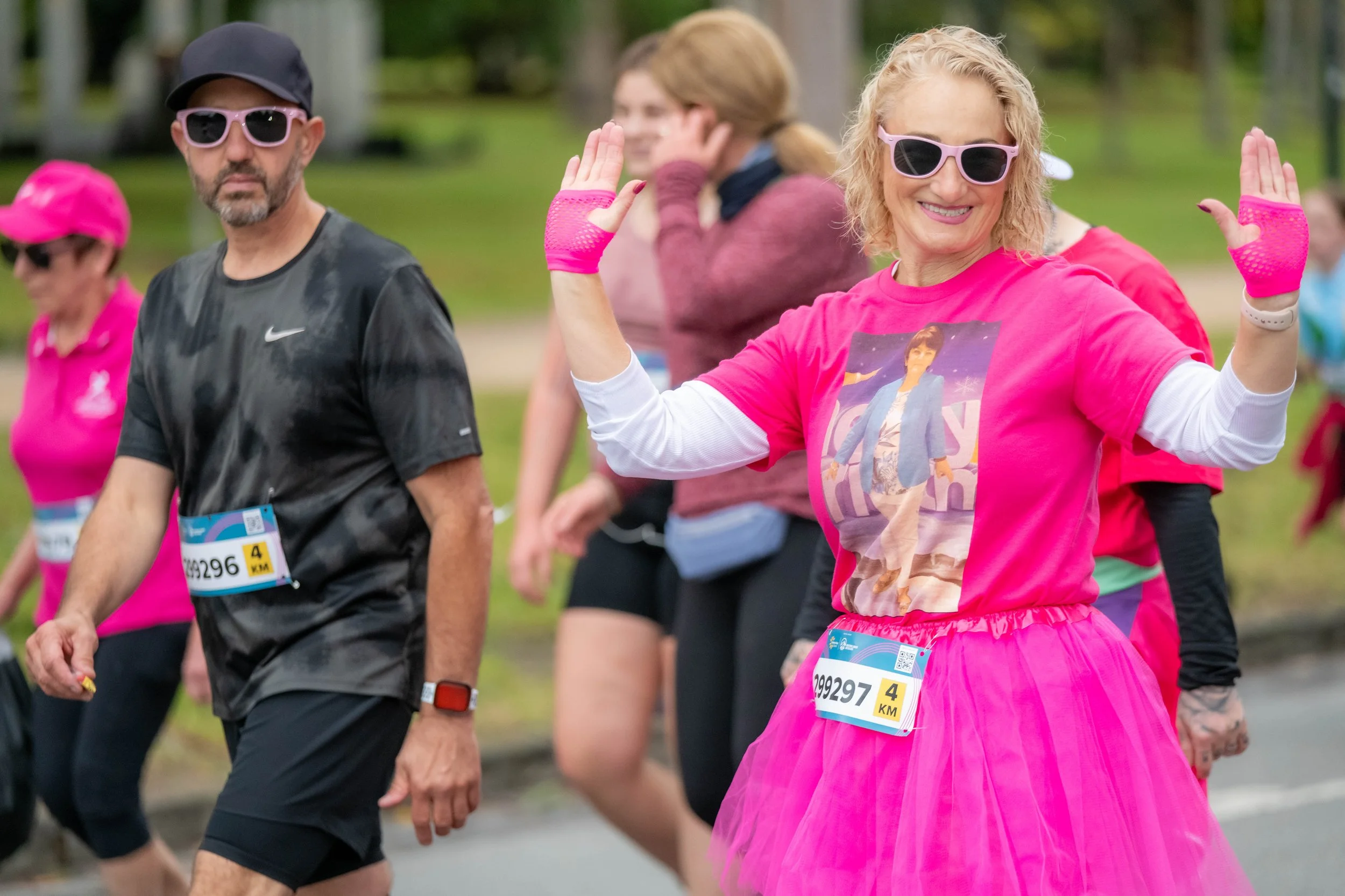 A racegoer in a pink tutu and memorial tee waves at the camera.