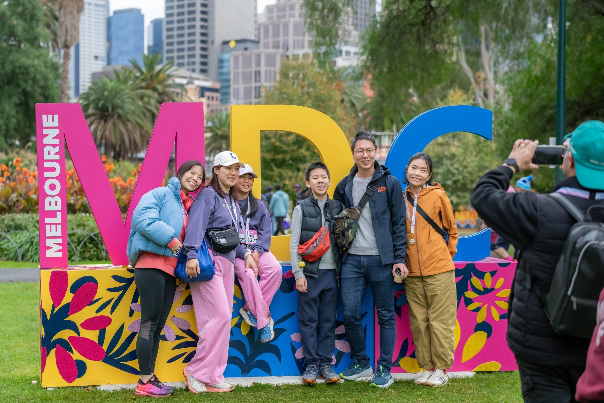A group of racegoers pose in front of the MDC sign. The city can be seen in the background.