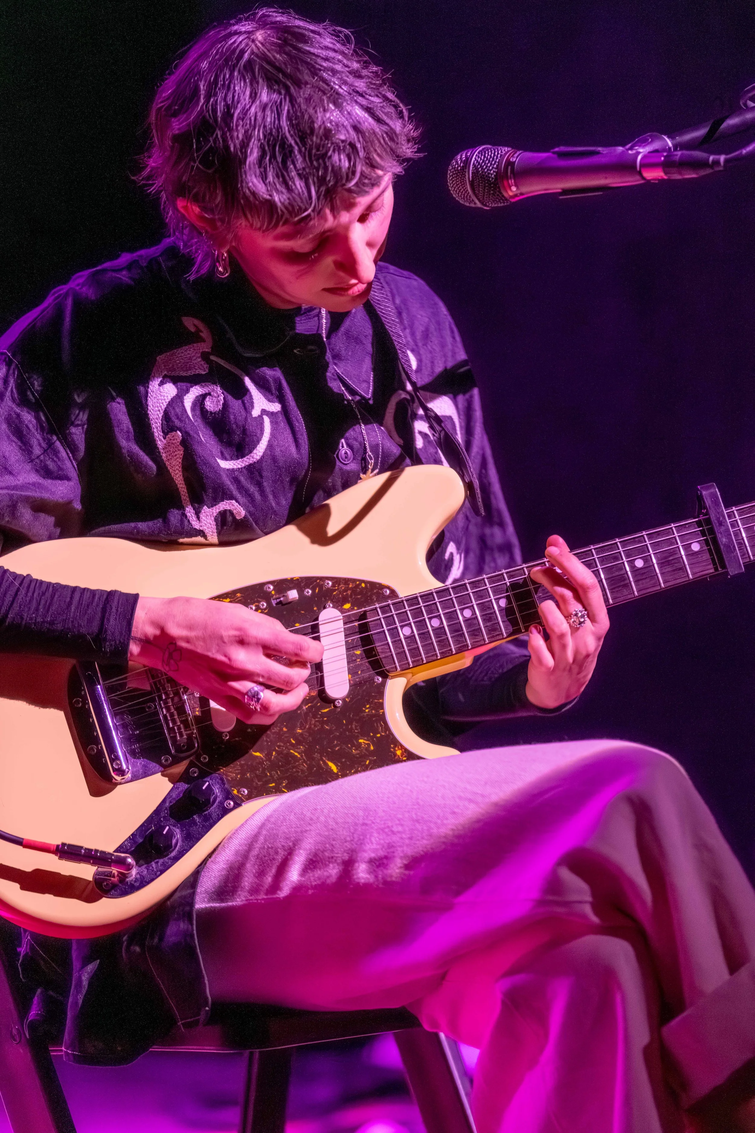 A human sits, looking at their guitar as they play.