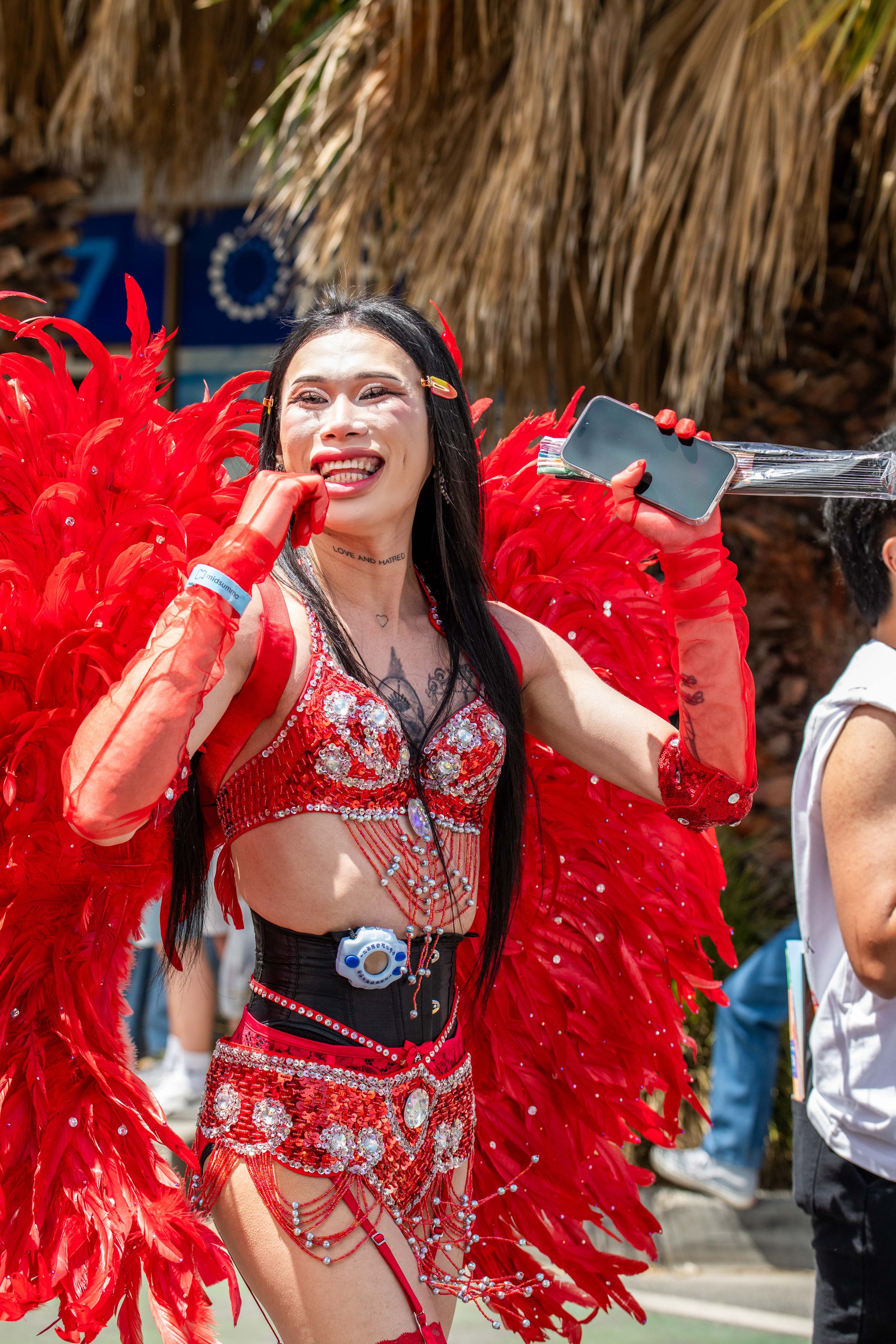 A human with red bejewelled bra and red wings smiles at the crowd.
