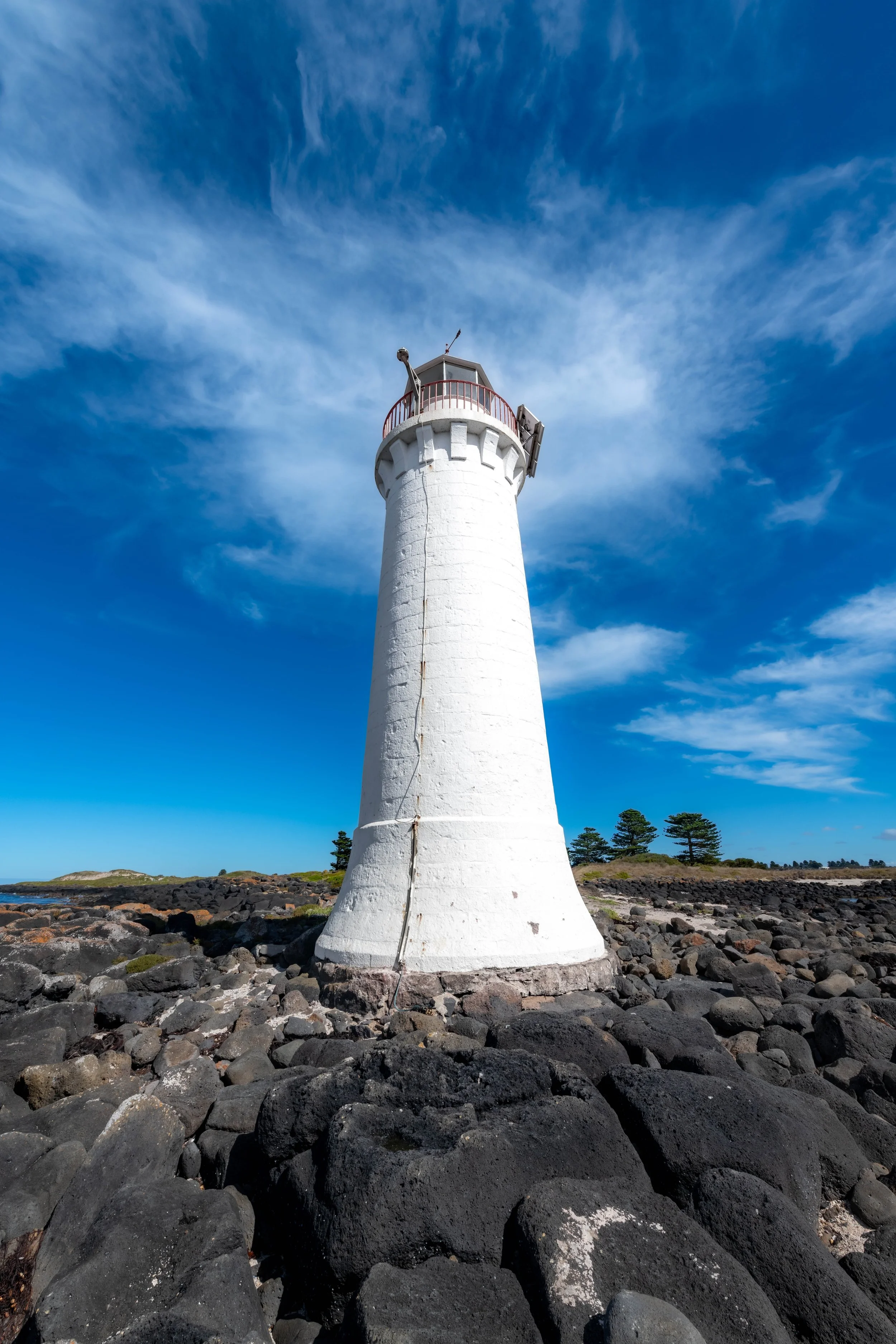 A white lighthouse sticking up out of black rocks.