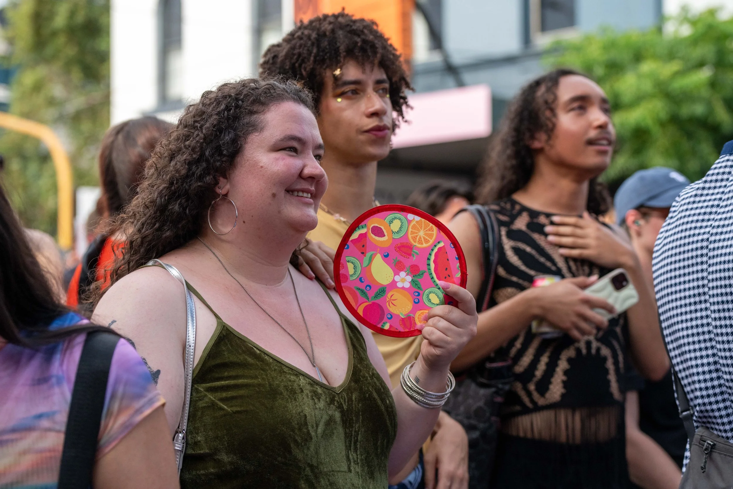 Crowd members smile. One holds a fruity fan.