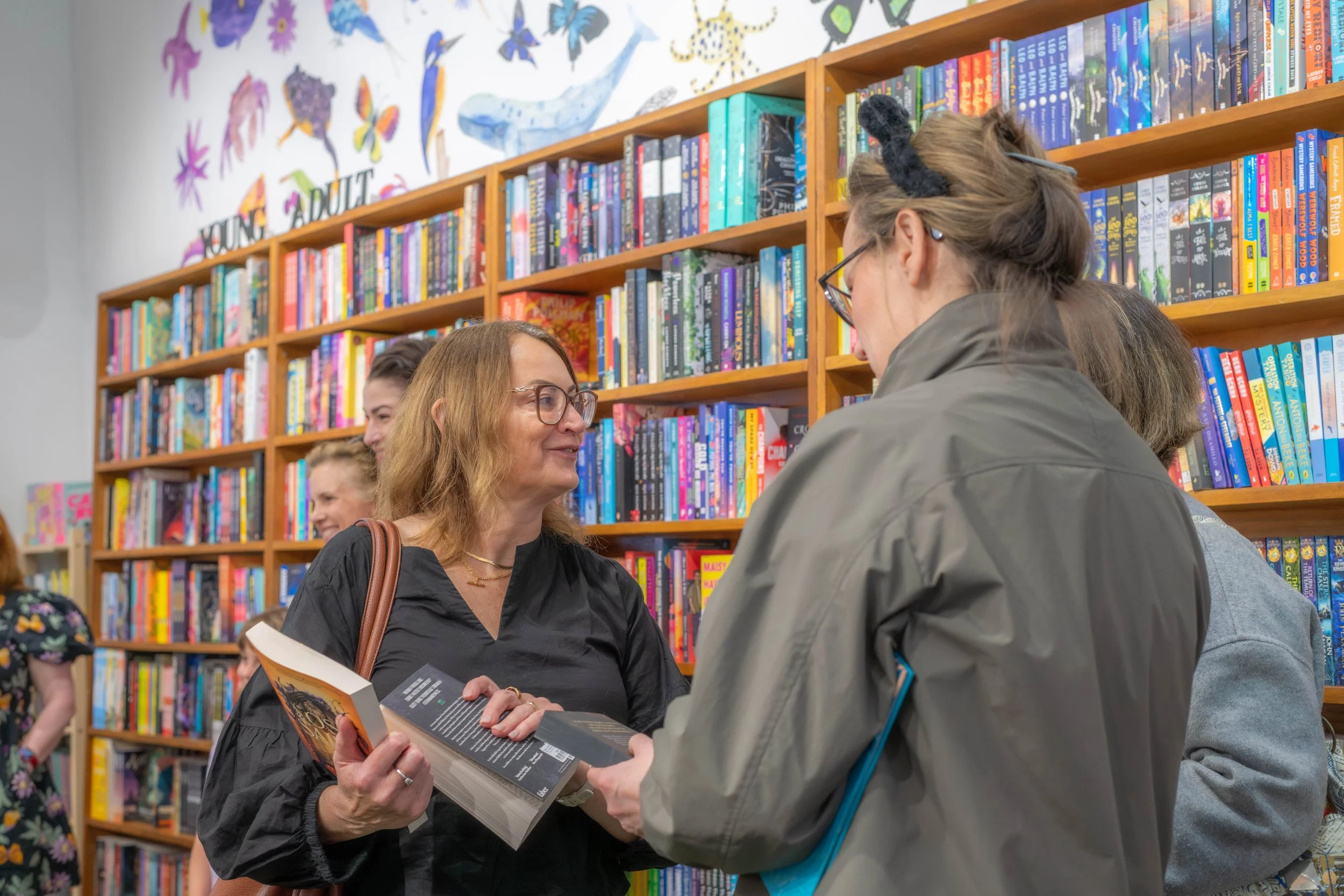 Three humans hold books and chat.