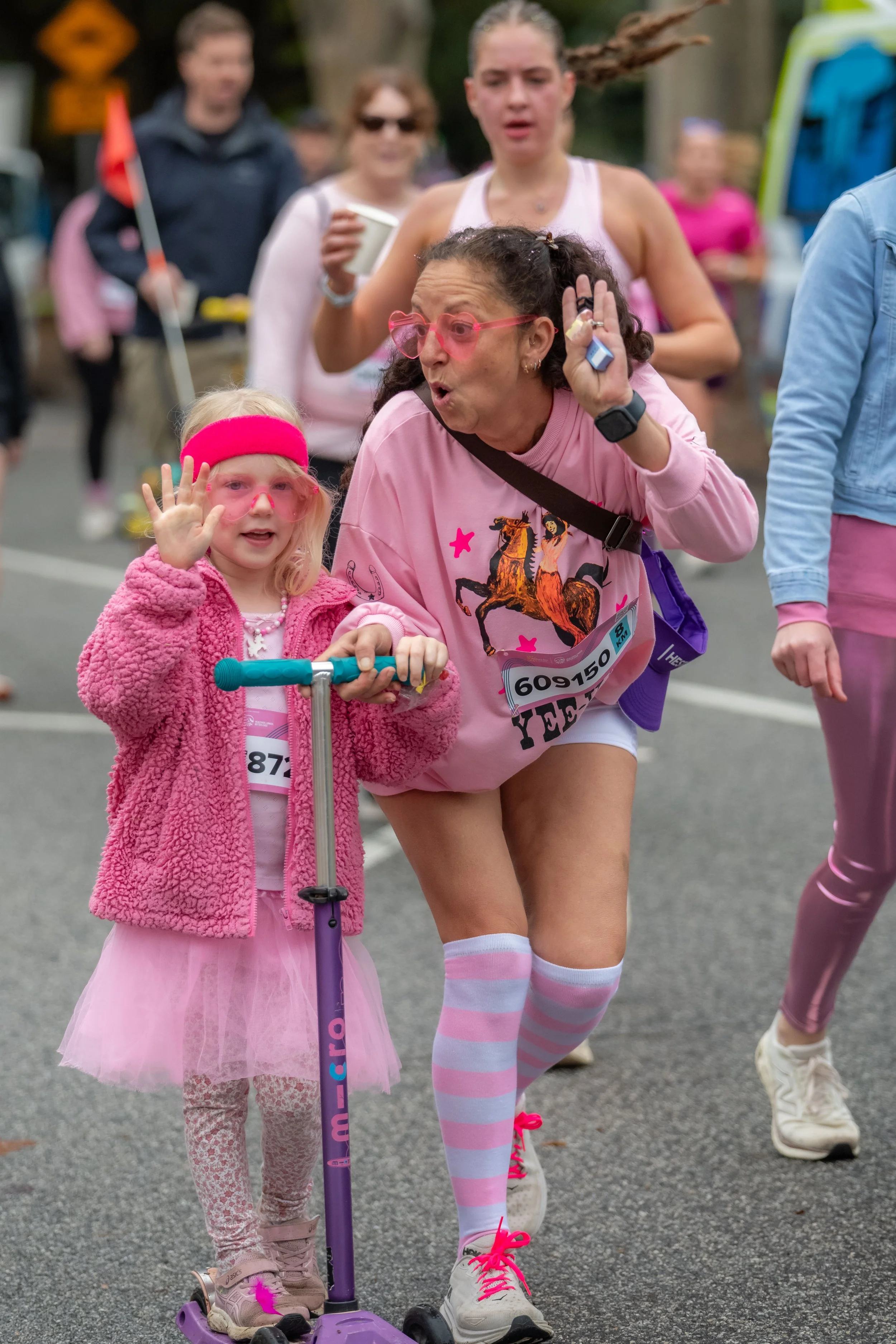 An adult racegoer poses with a child on a scooter.