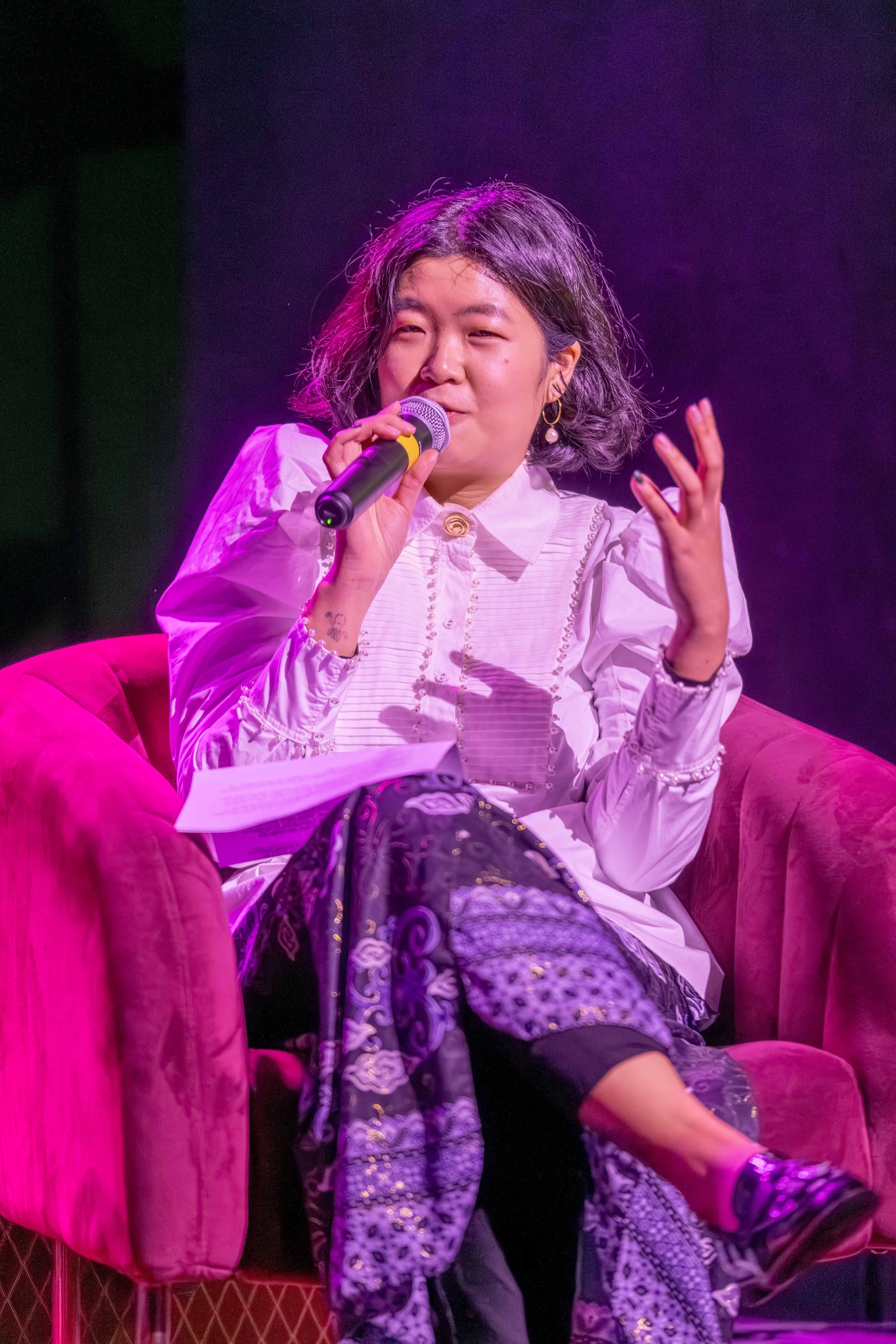 A human speaks into the microphone whilst looking at an unseen audience.
