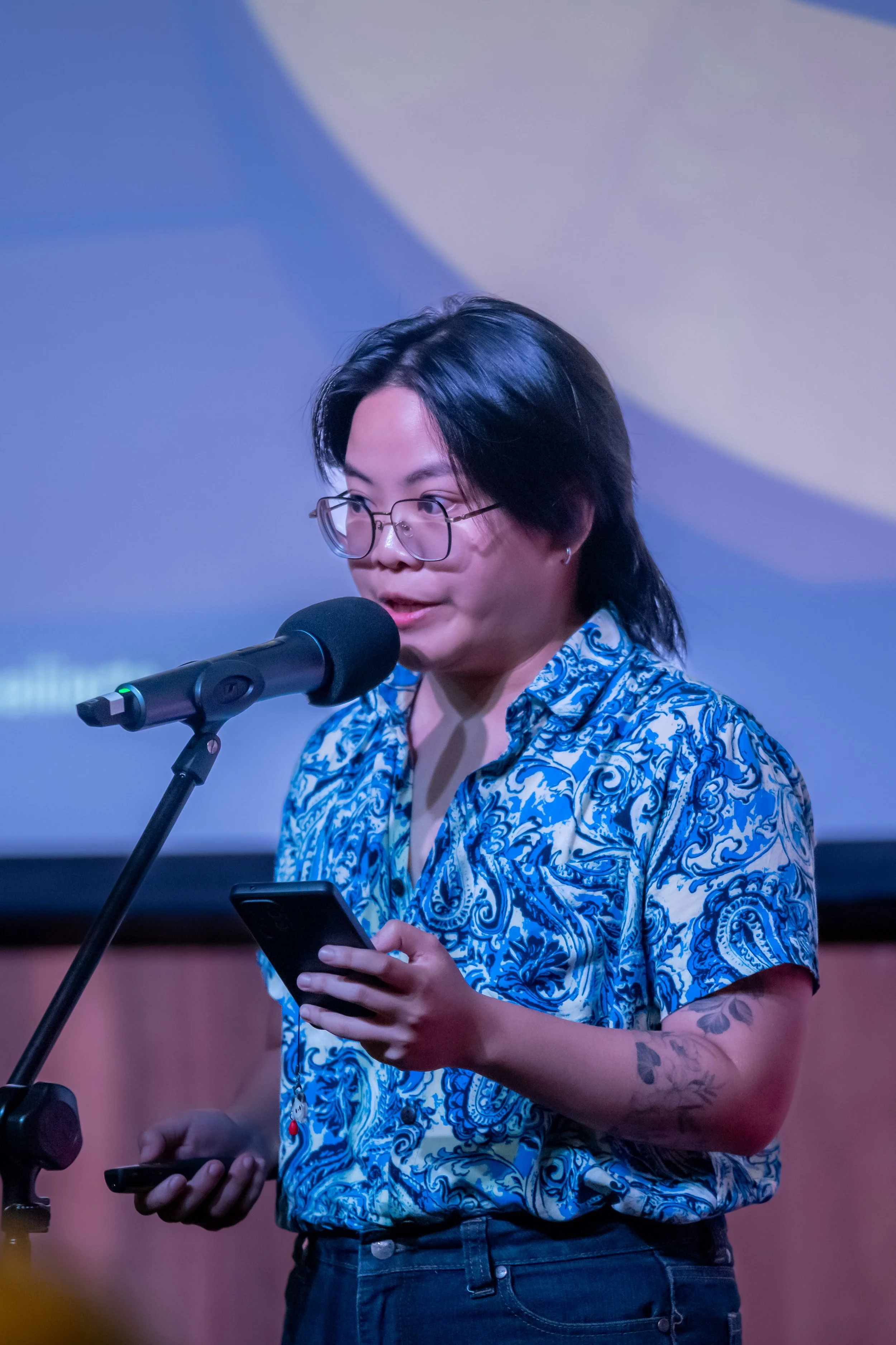 A human in a blue and white shirt speaks into a microphone.