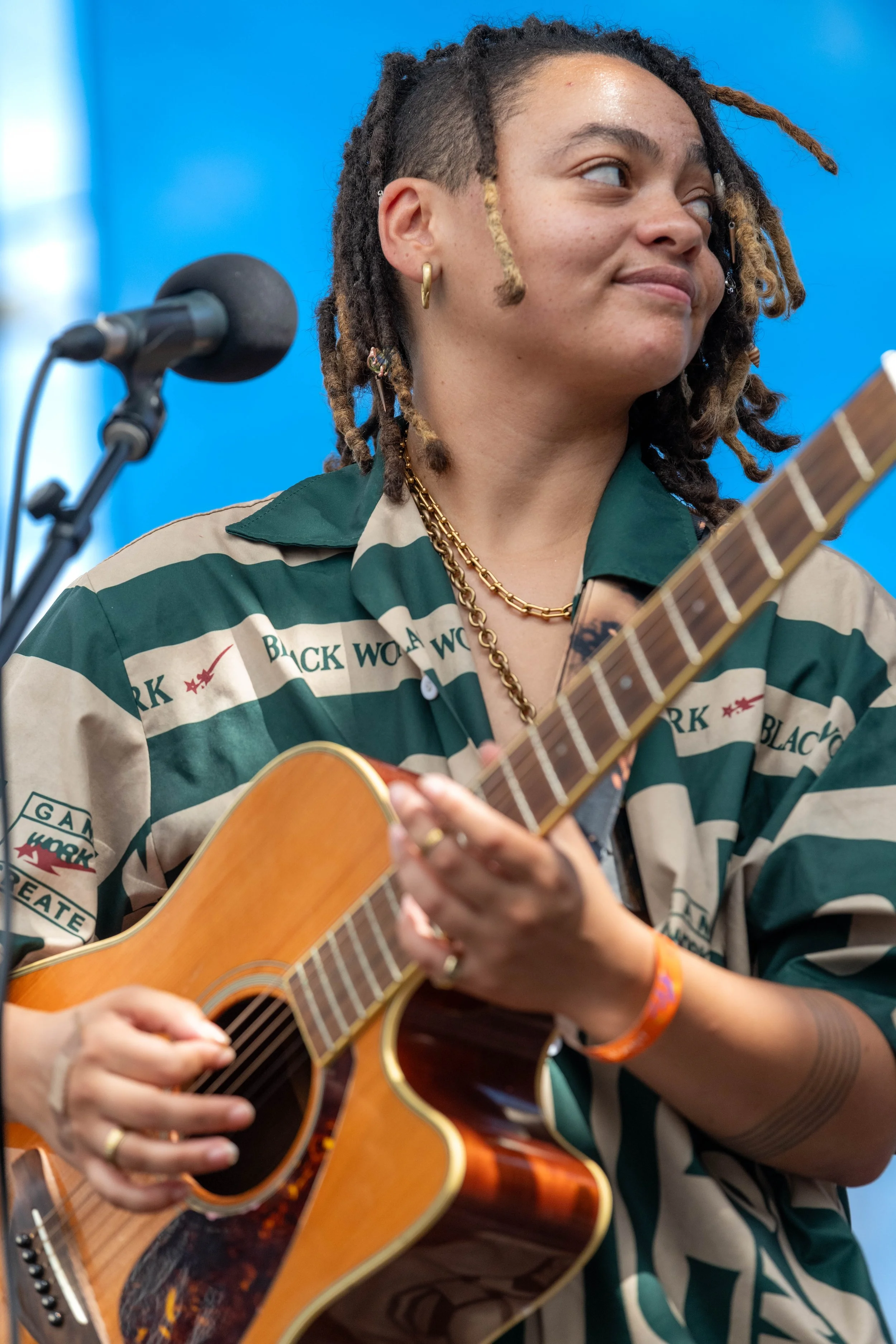 Malaika Mfalme looks to their left as they play the guitar.