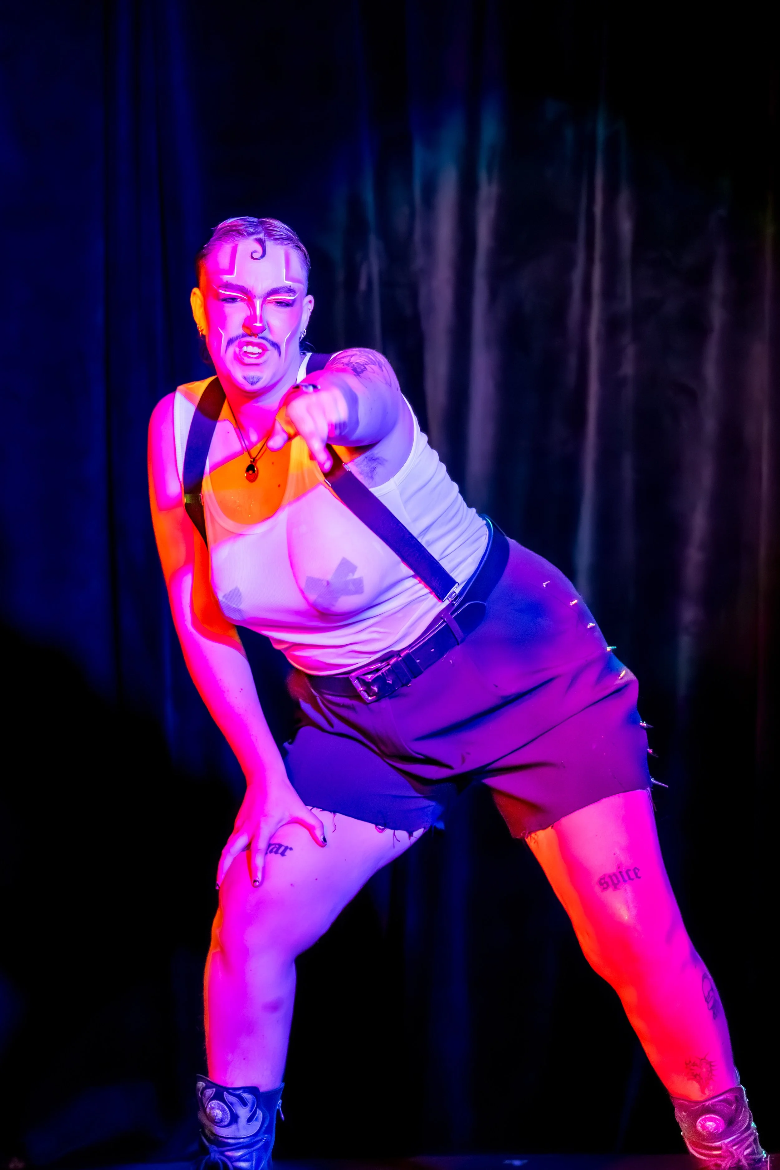 A drag king bends over and points to the camera.