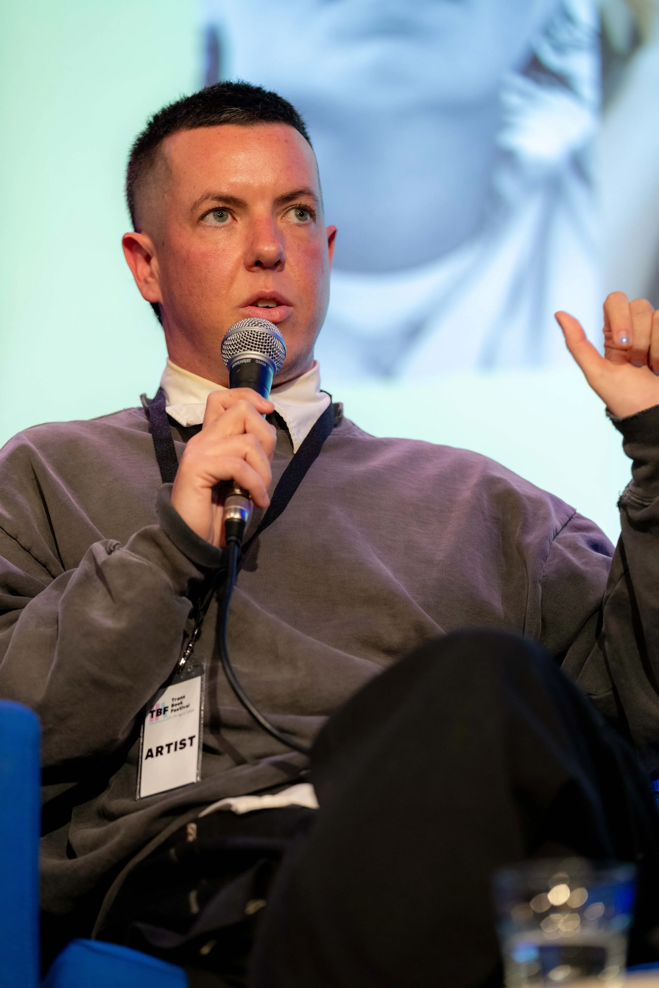 A panelist in a grey jumper speaks into a microphone.
