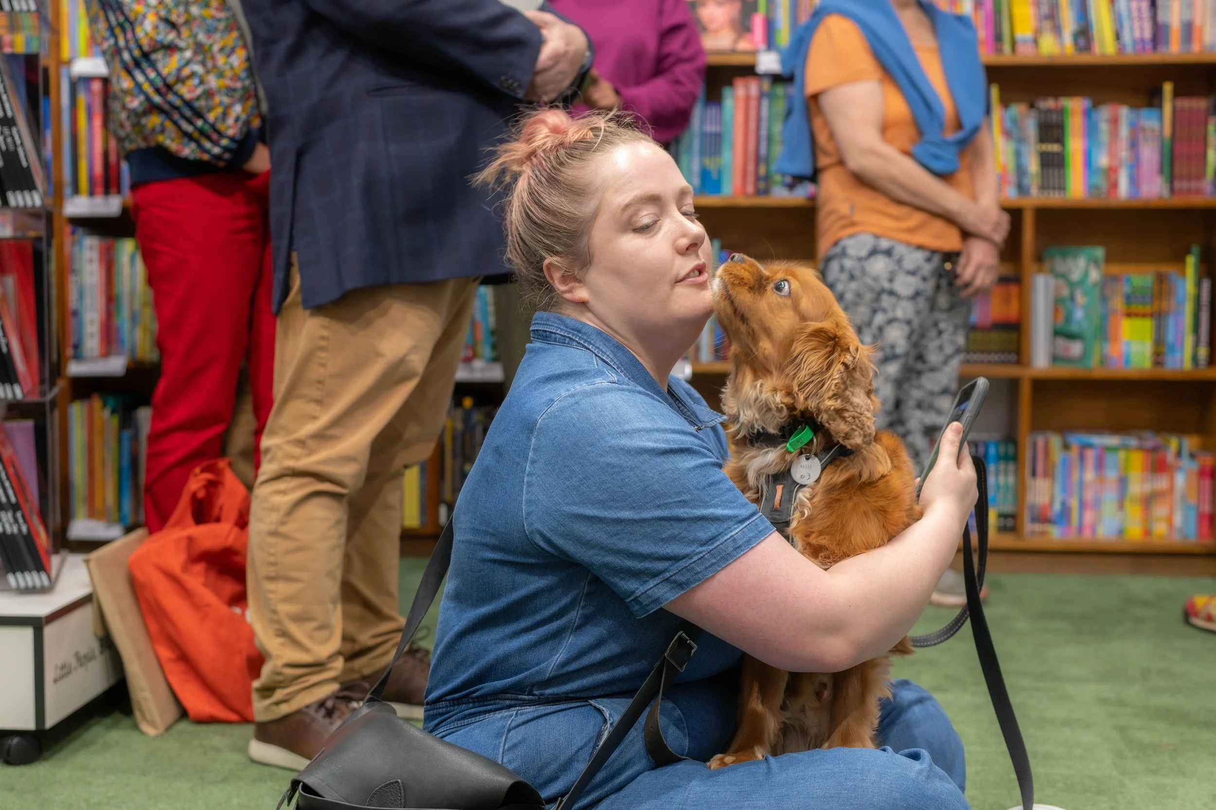 A human sits as a dog licks their face.