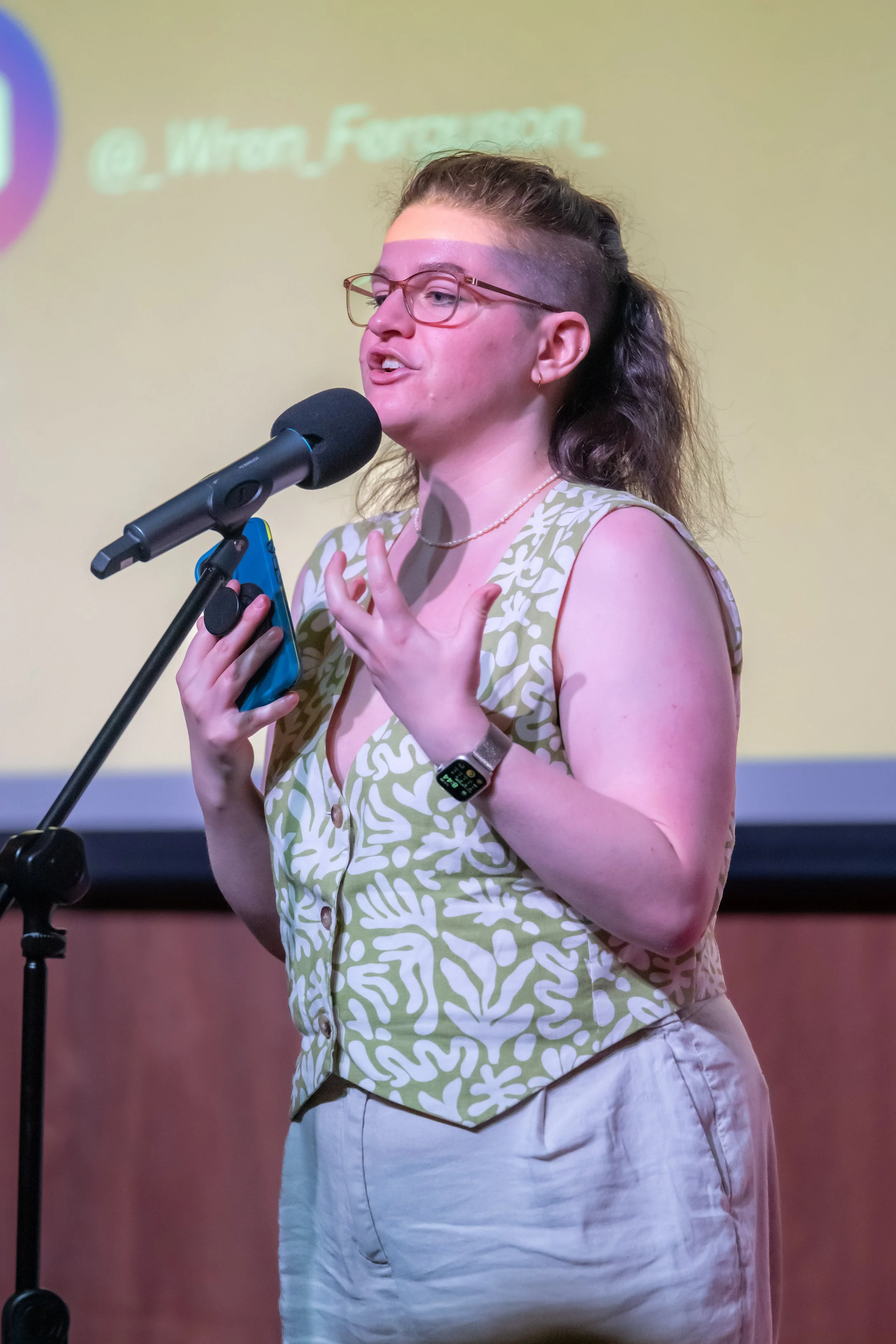 A human in a waistcoat speaks into a microphone.