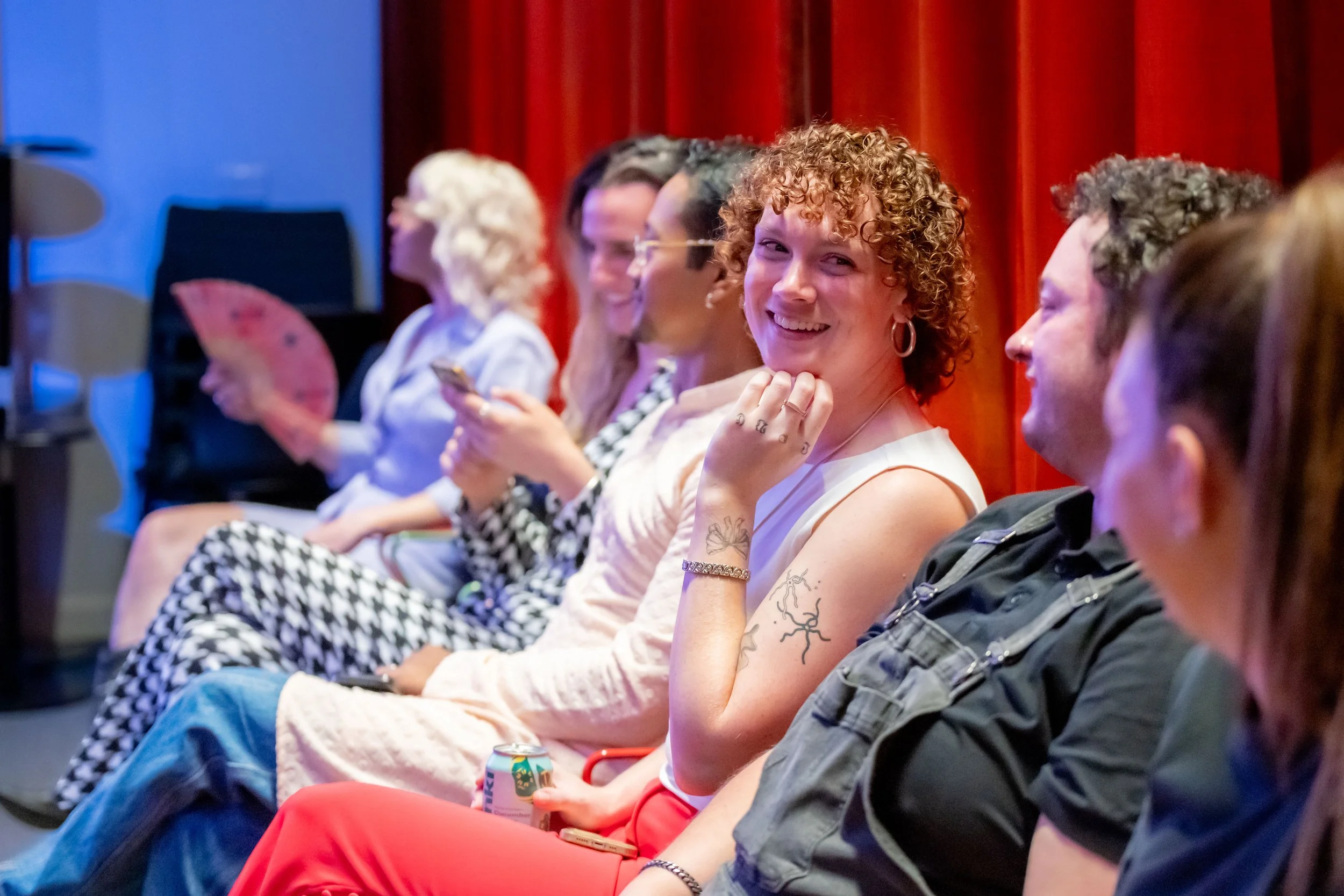 A human with curly hair raises their hand to their face and smiles at the human next to them.