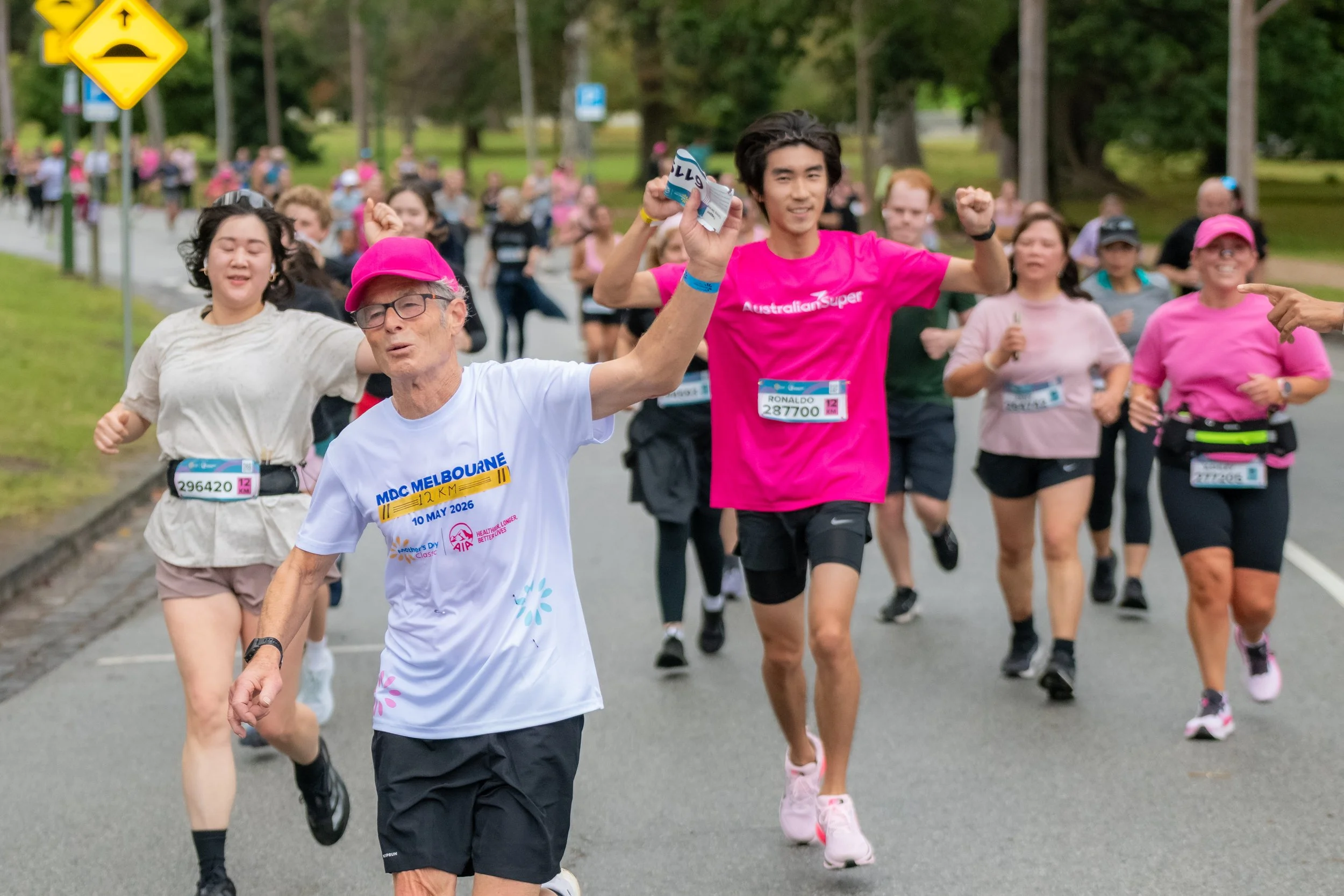 A racegoer in a pink hat waves at the camera whilst runniing.