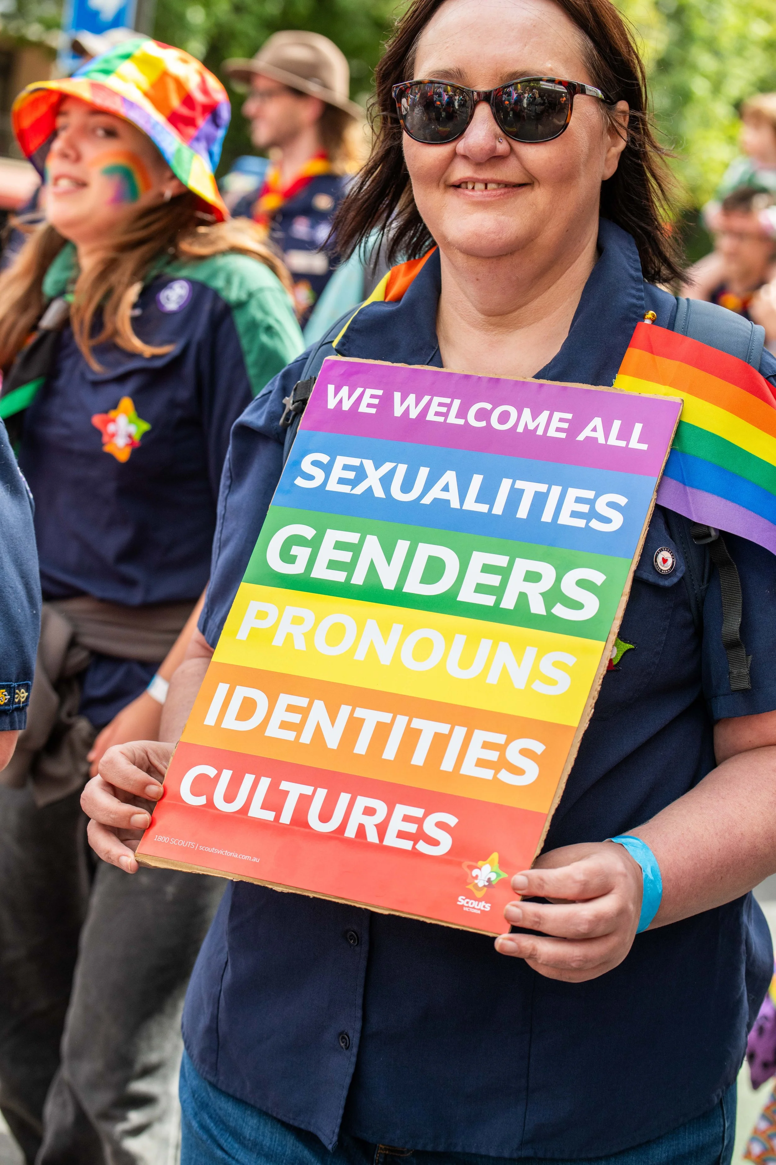 A human holding a sign "We welcome all sexualities, genders, pronouns, identities, cultures".