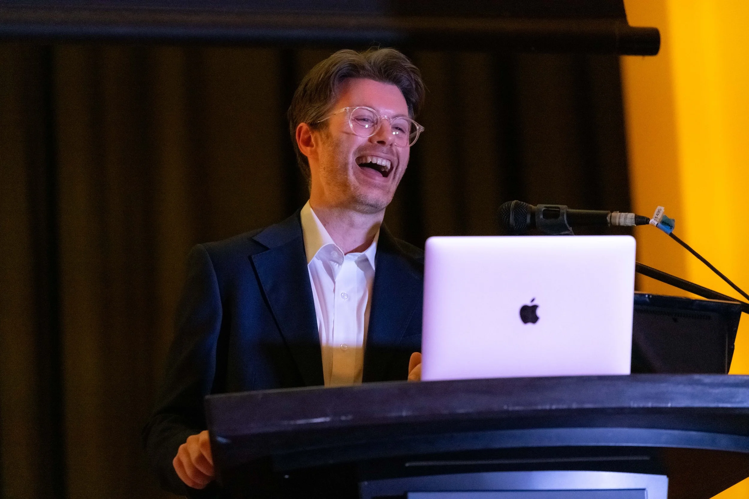 Damien O'Meara laughing from behind a lecturn.