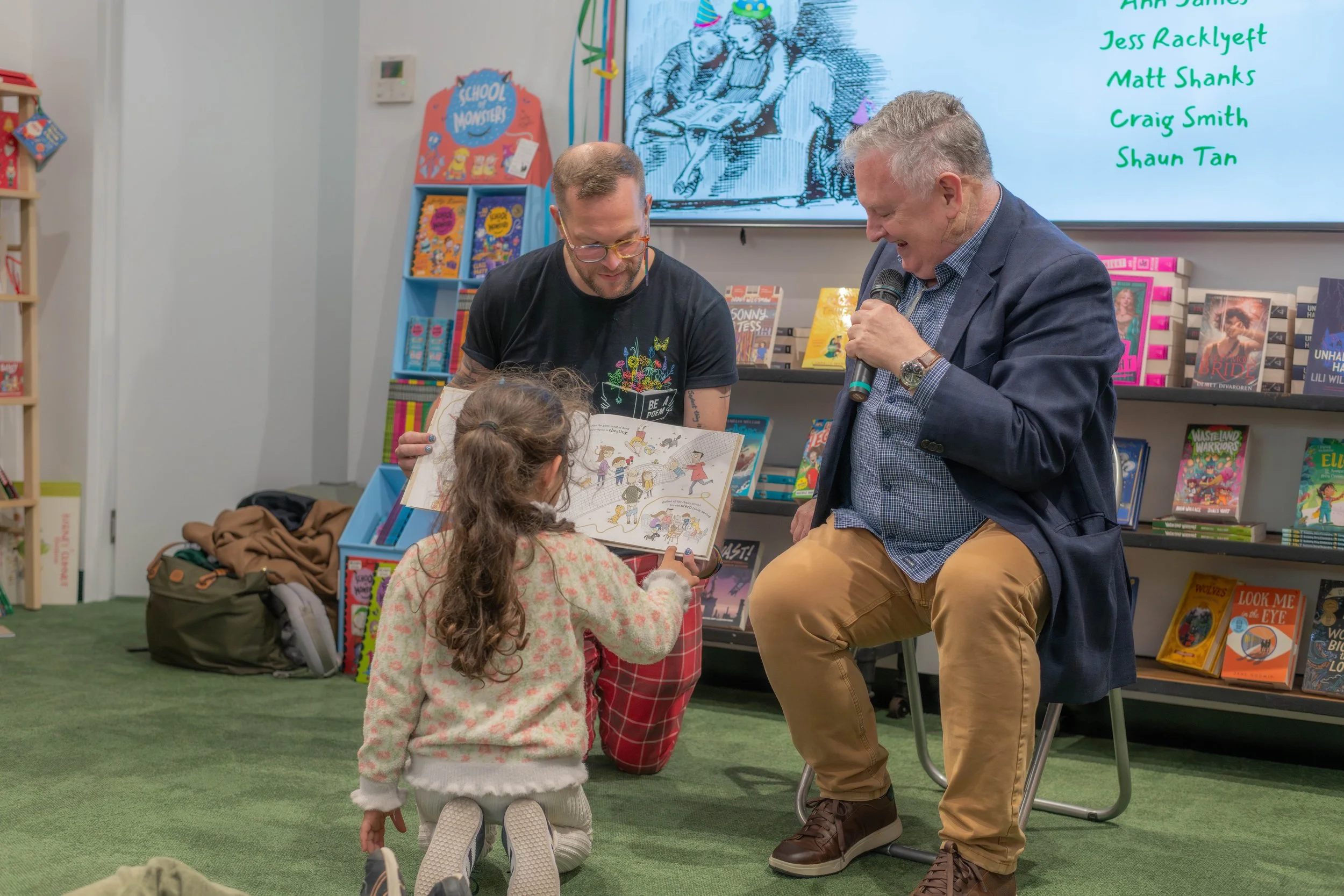 An author gives storytime as Michael Earp holds the book. A young child points to a spot on the page.