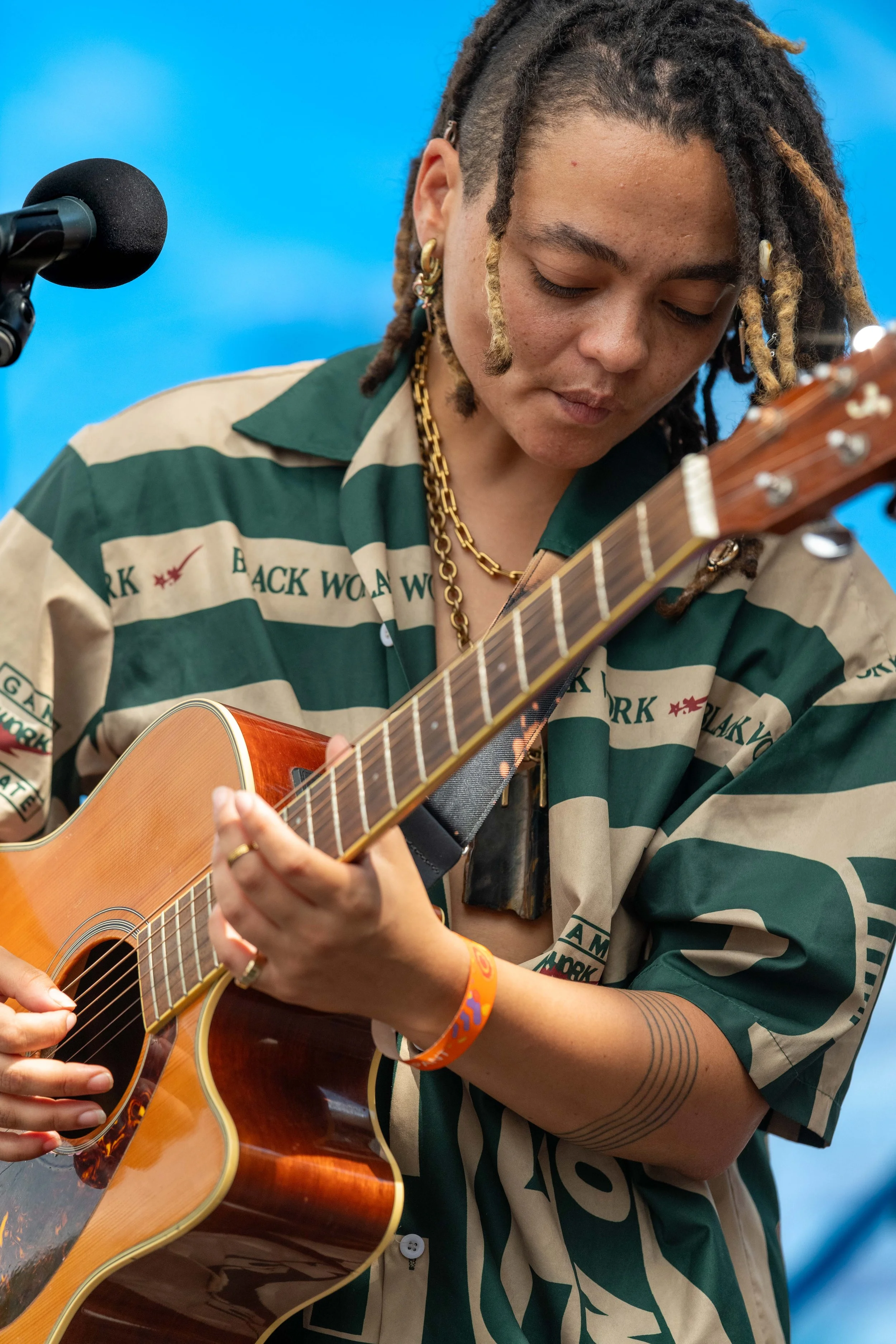 Malaika Mfalme looks down as they play the guitar.