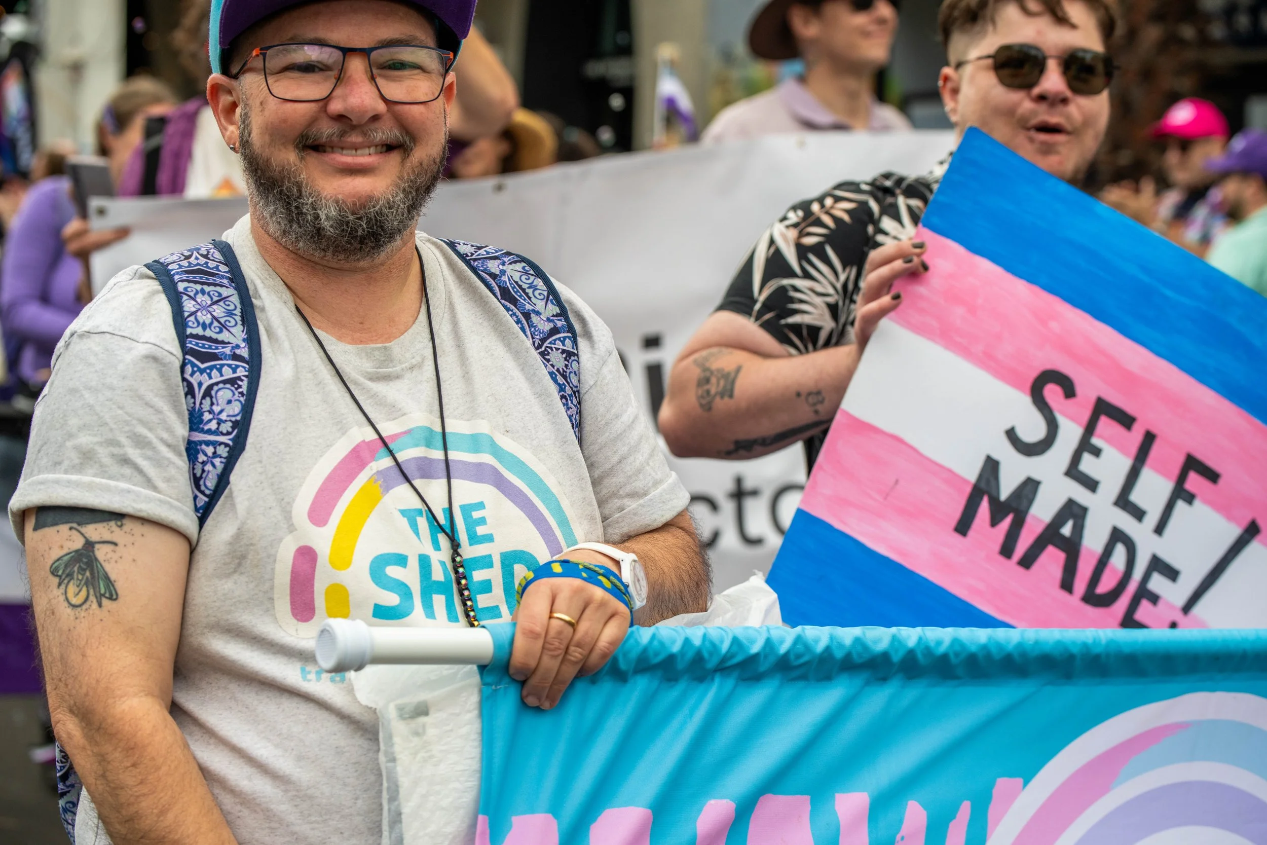 Two humans marching from The Shed. One is holding a sign "Self Made!".