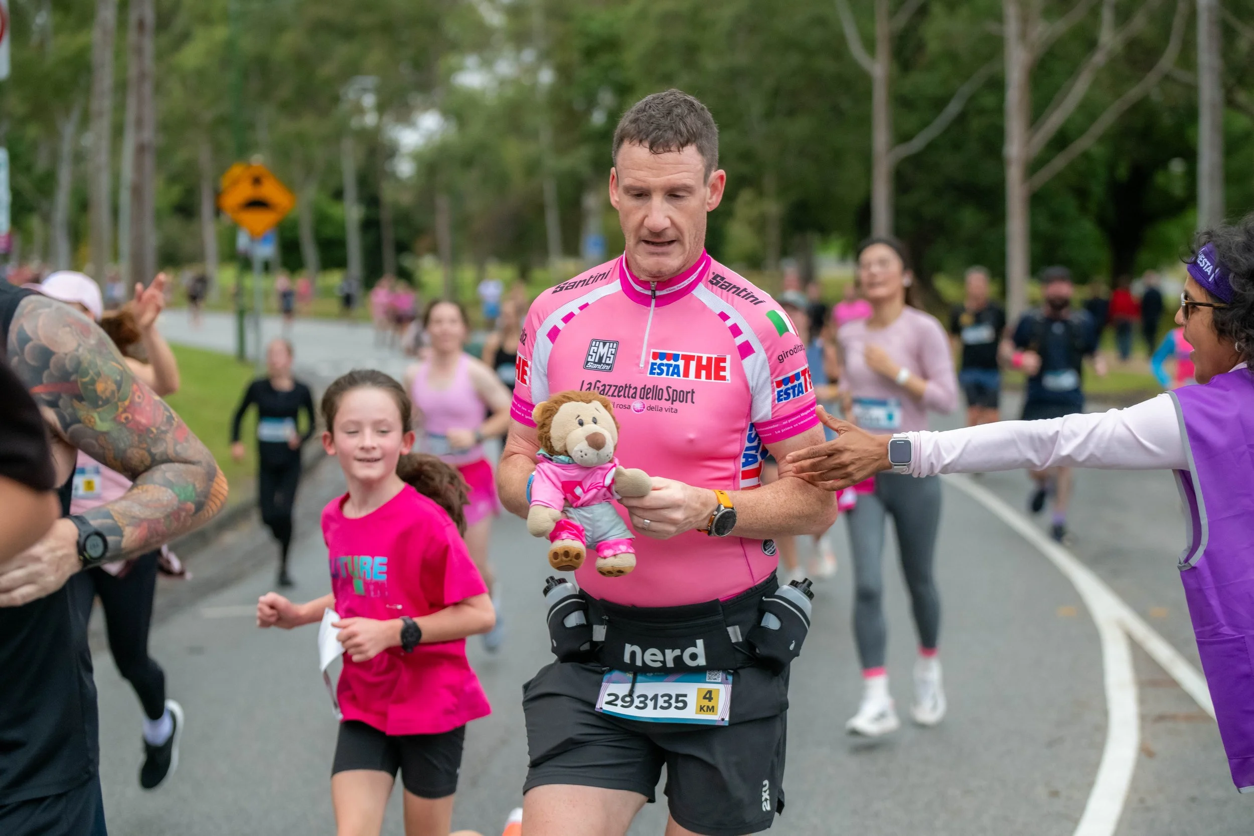 A racegoer holds a small teddy bear wearing pink.