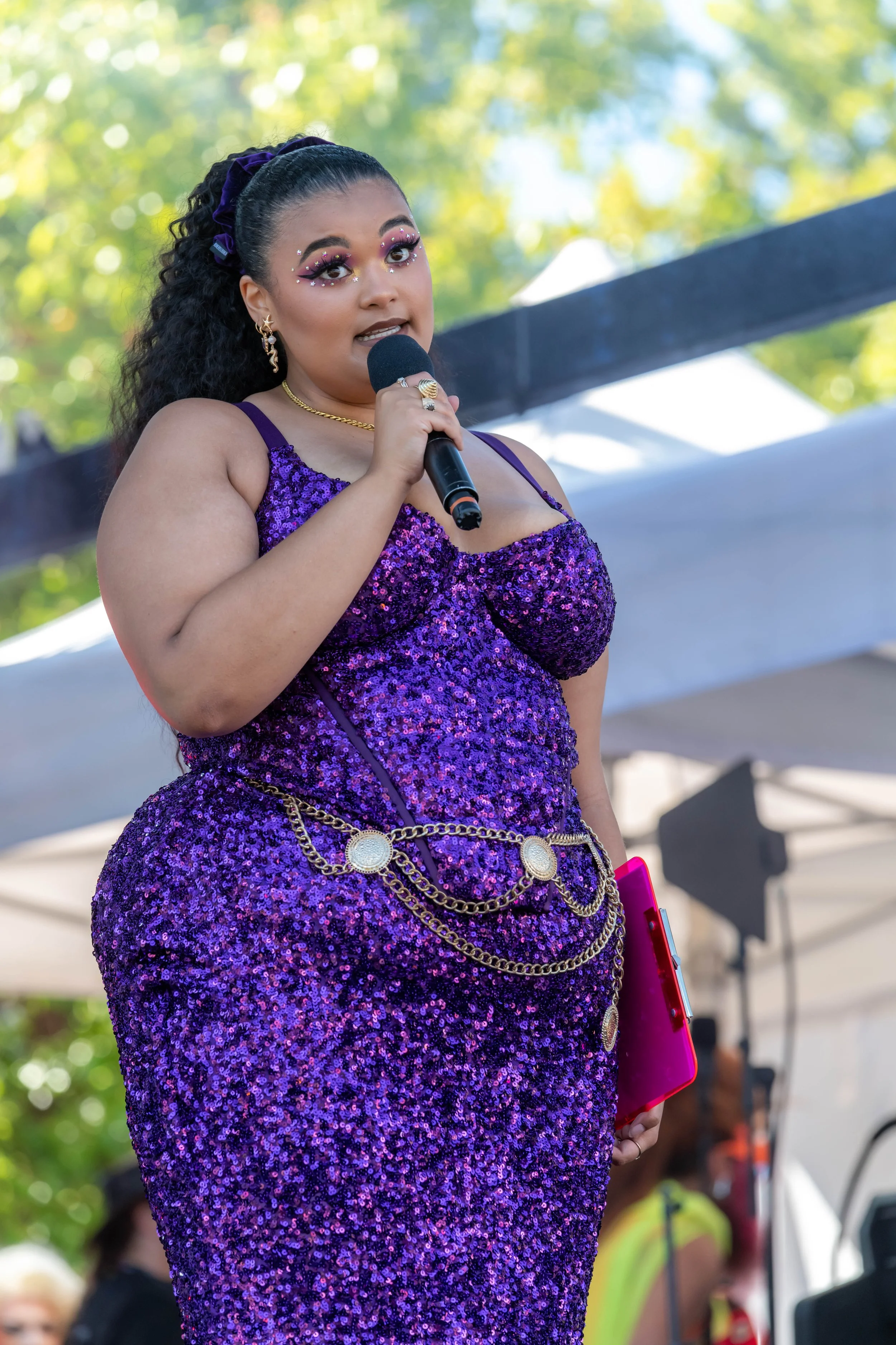 Milo Hartill wears a slinky purple dress as they speak into a microphone.