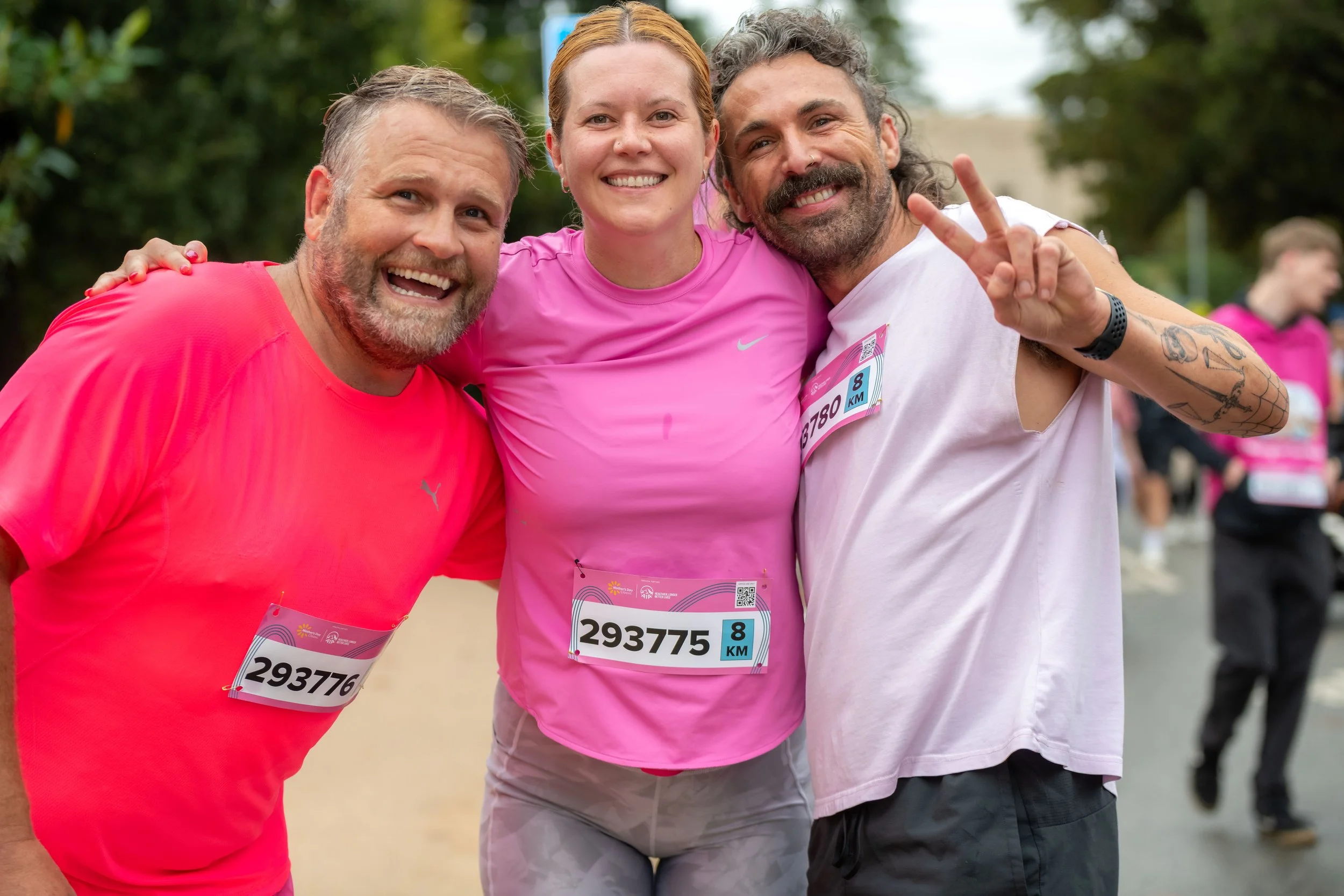 Three racegoers wear pink and smile for the camera.