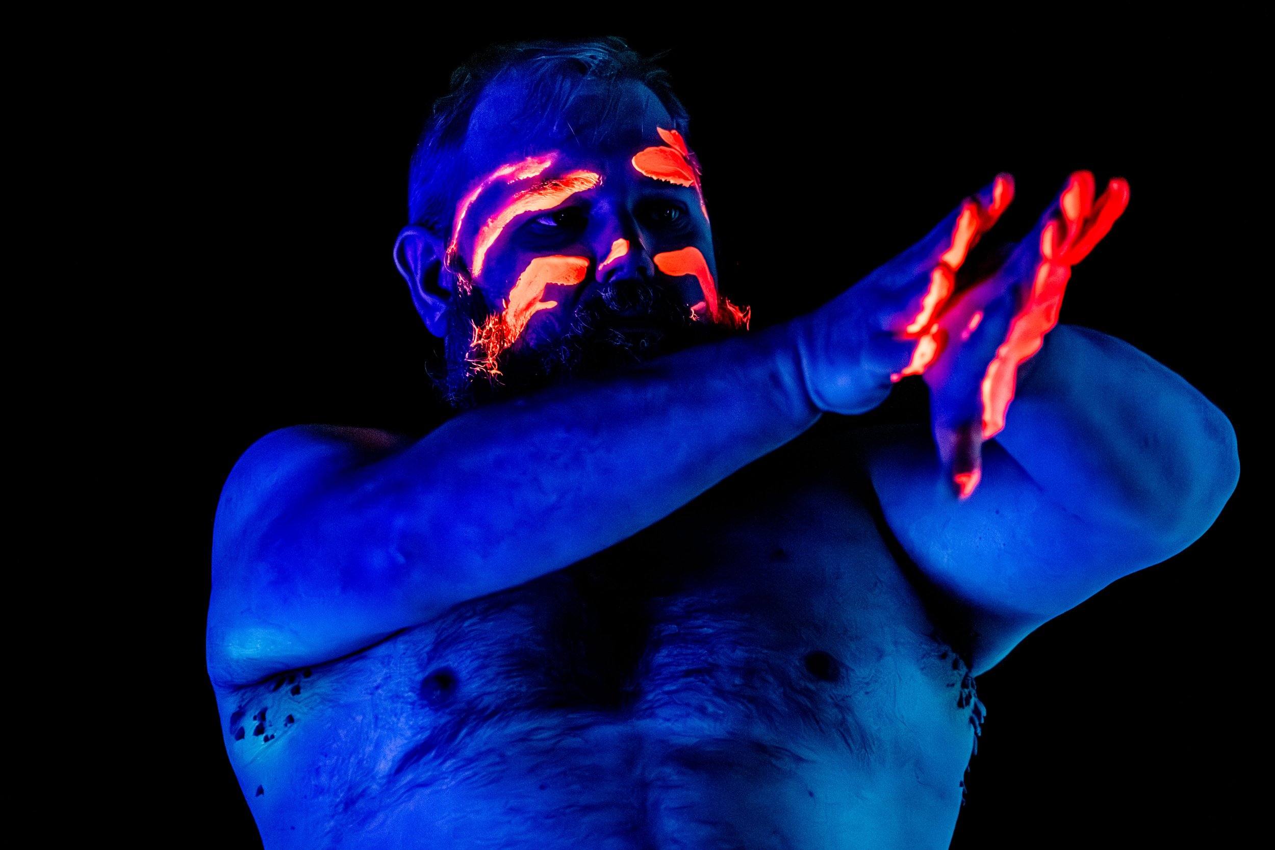 A performer with orange glow in the dark paint smeared across their face and on the palms of their hands.