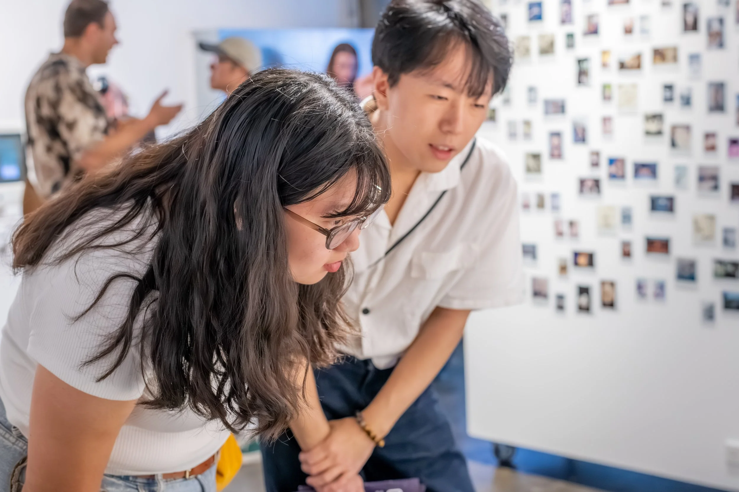 Two humans bend over to look at artwork.