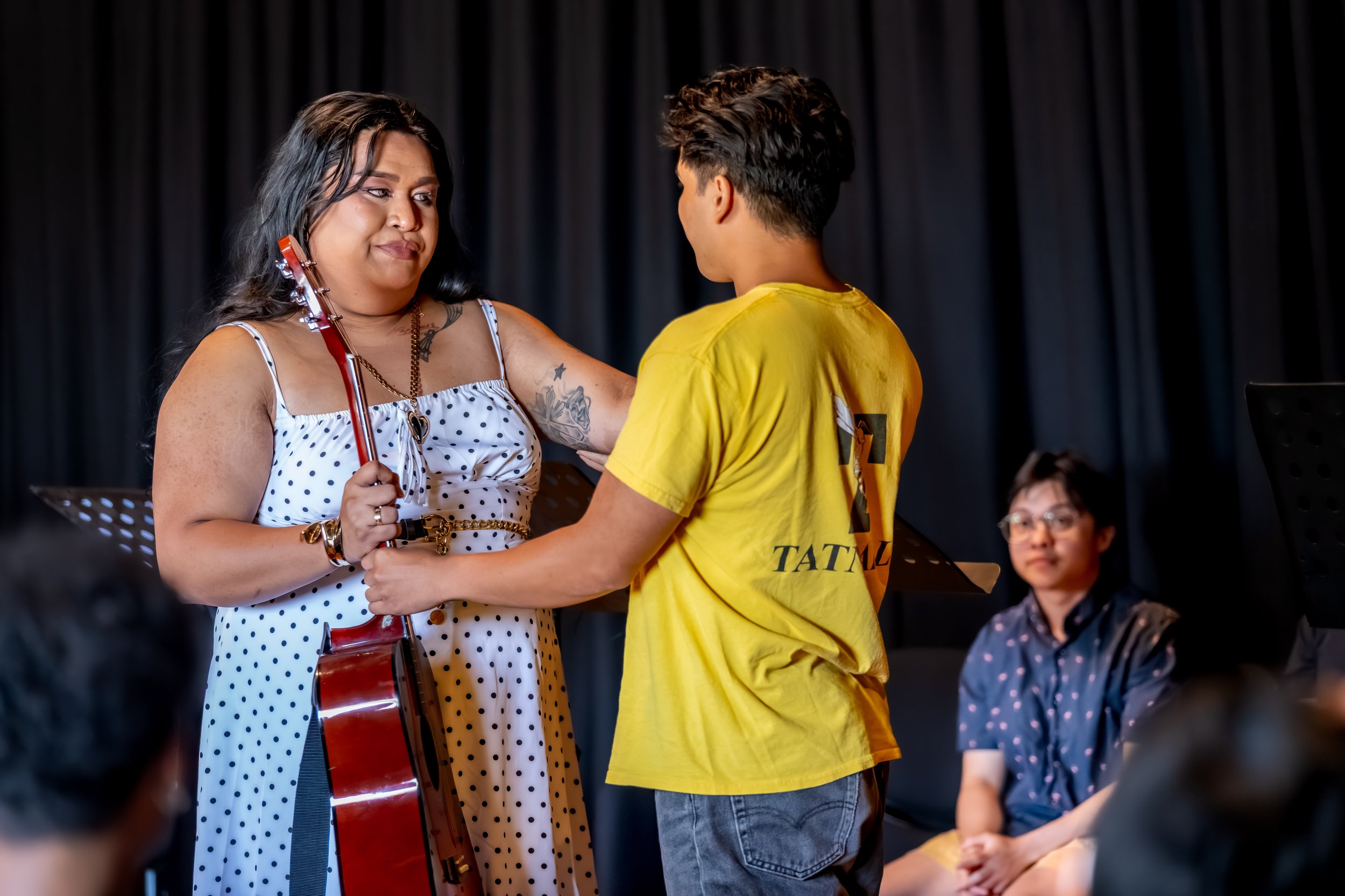 A human hands a guitar over to another human.