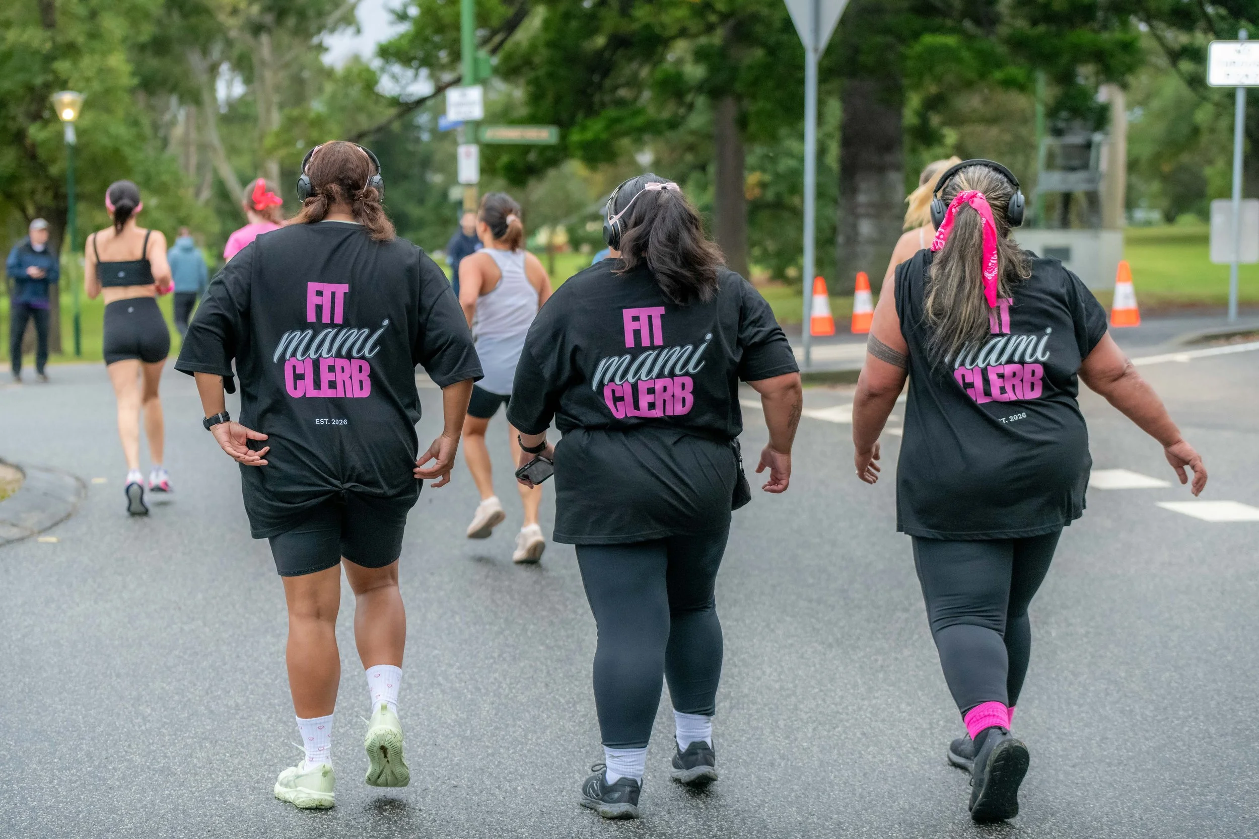 Three racegoers wear black tees with "Fit Mami Clerb" written on the back.
