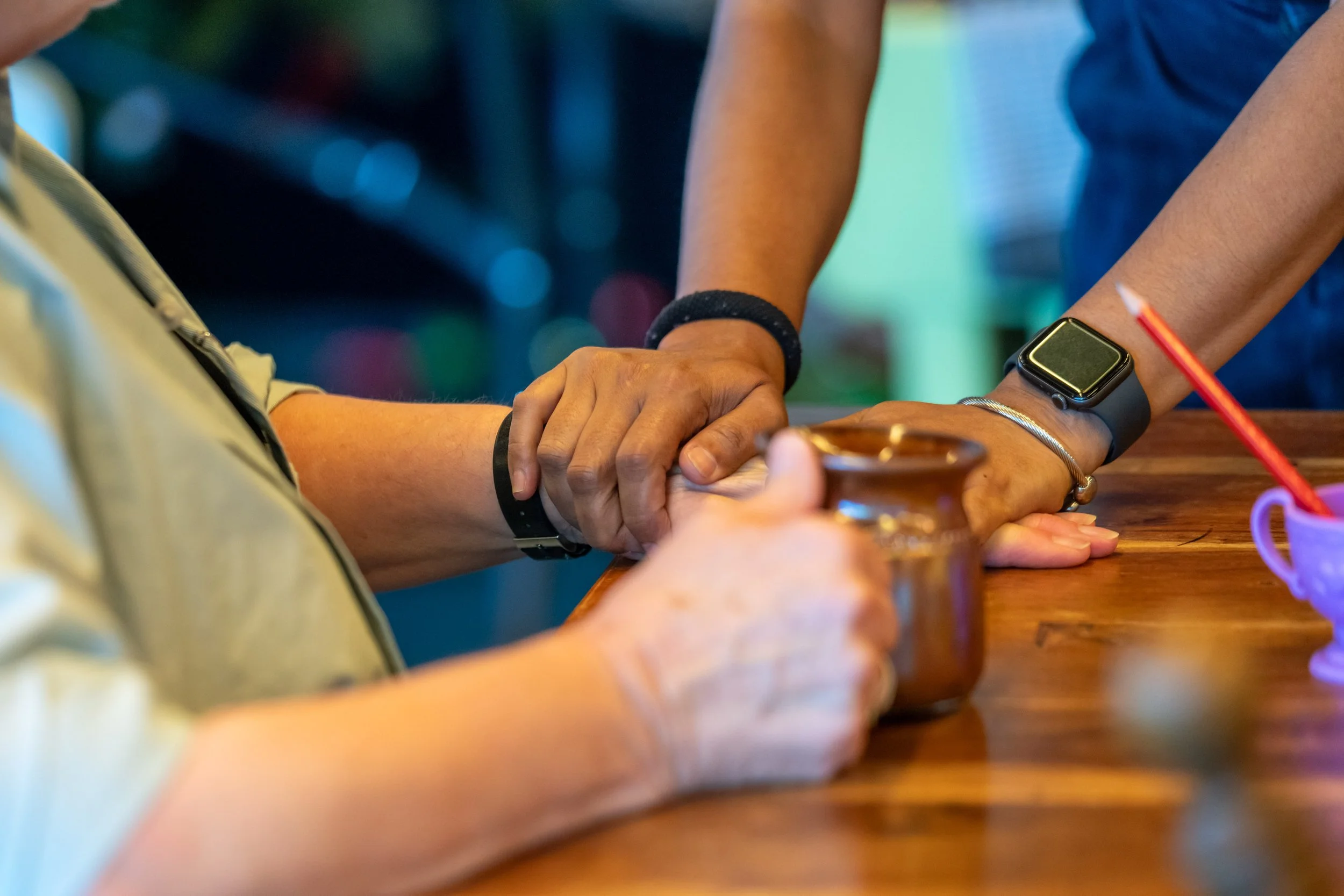 A hand holds a mug. Two hands hold onto an arm.