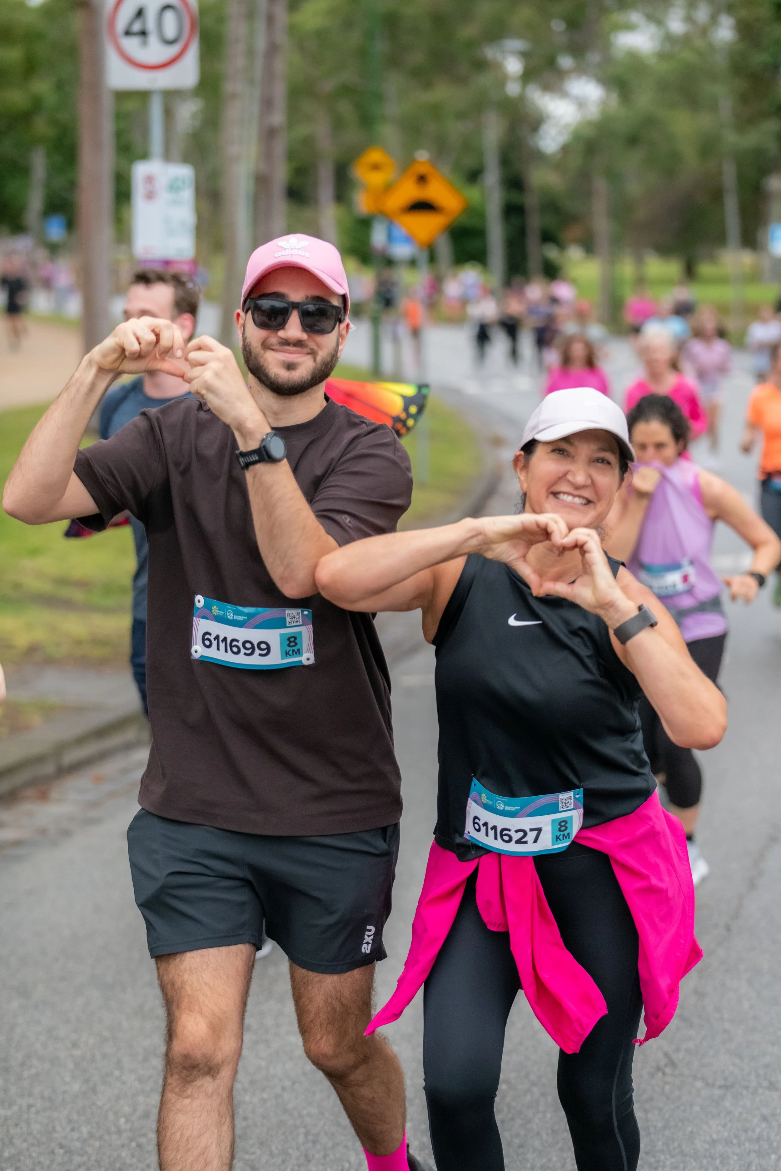 Two racegoers hold up the heart symbol with their hands.