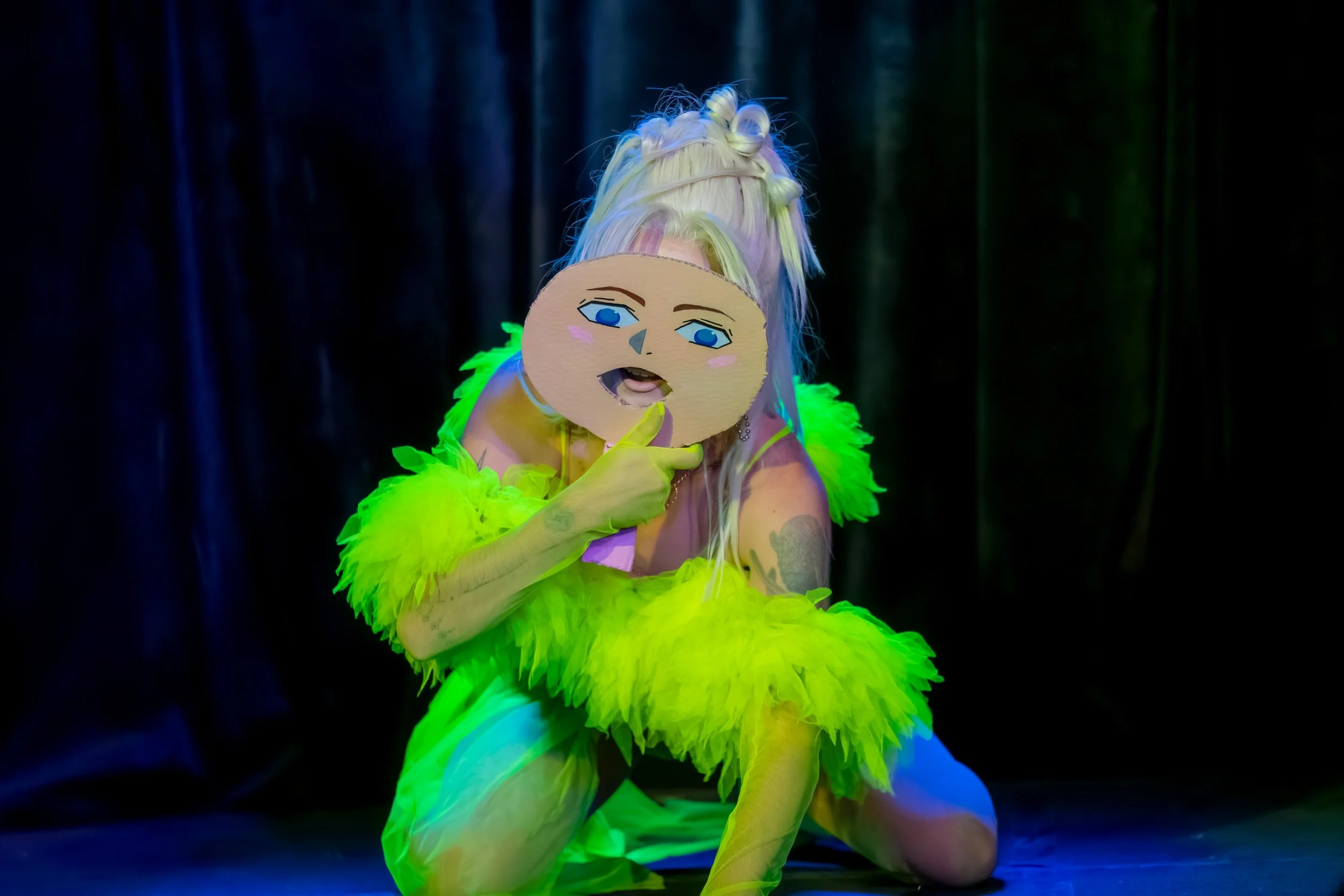 A human in neon holds up a white mask in front of their face.