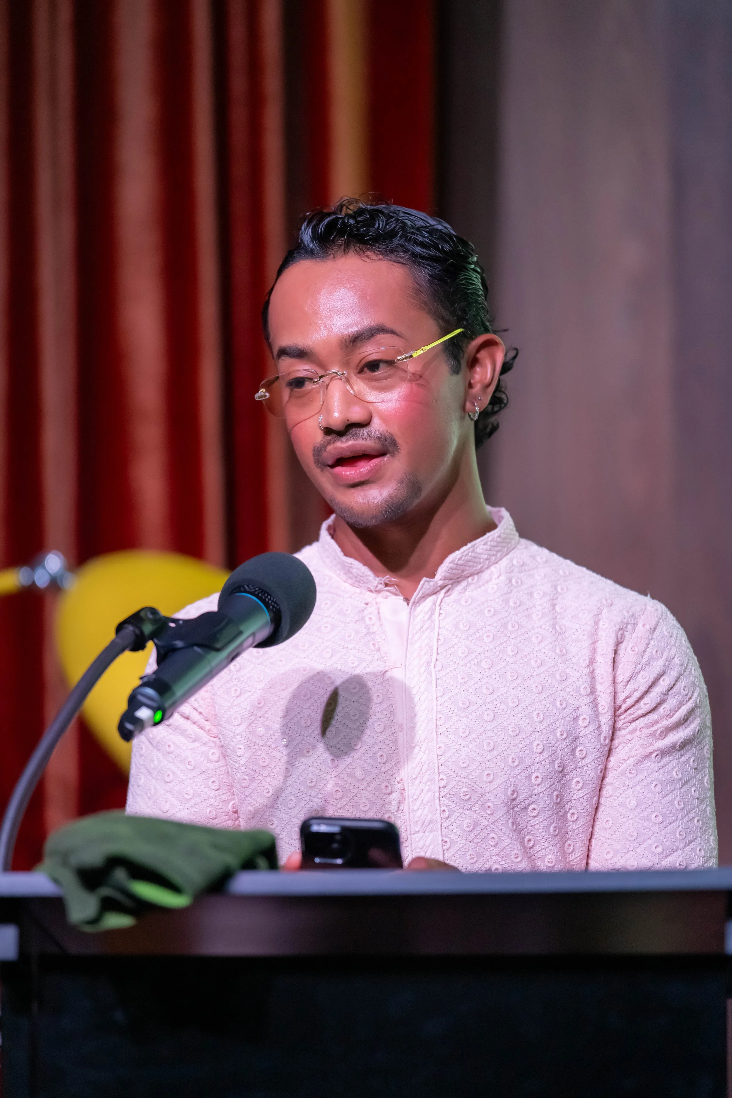 A human wearing white speaks into a microphone at a lecturn.