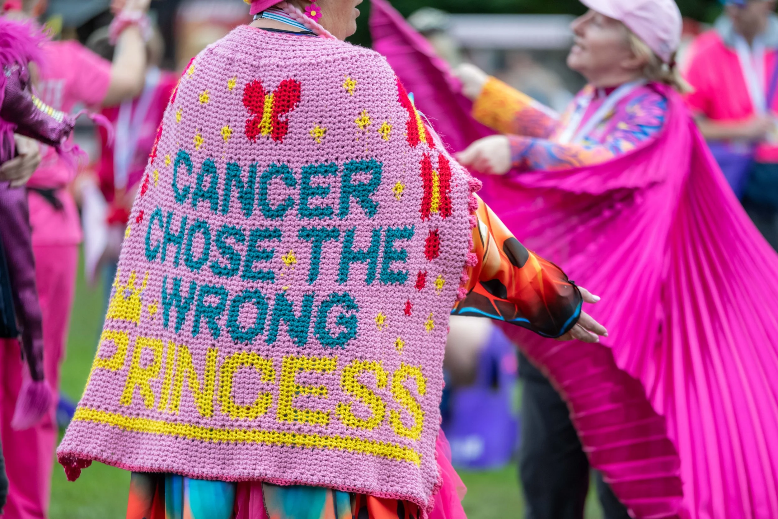 A racegoer wears a knitted cape with "Cancer chose the wrong princess" stitched into it.
