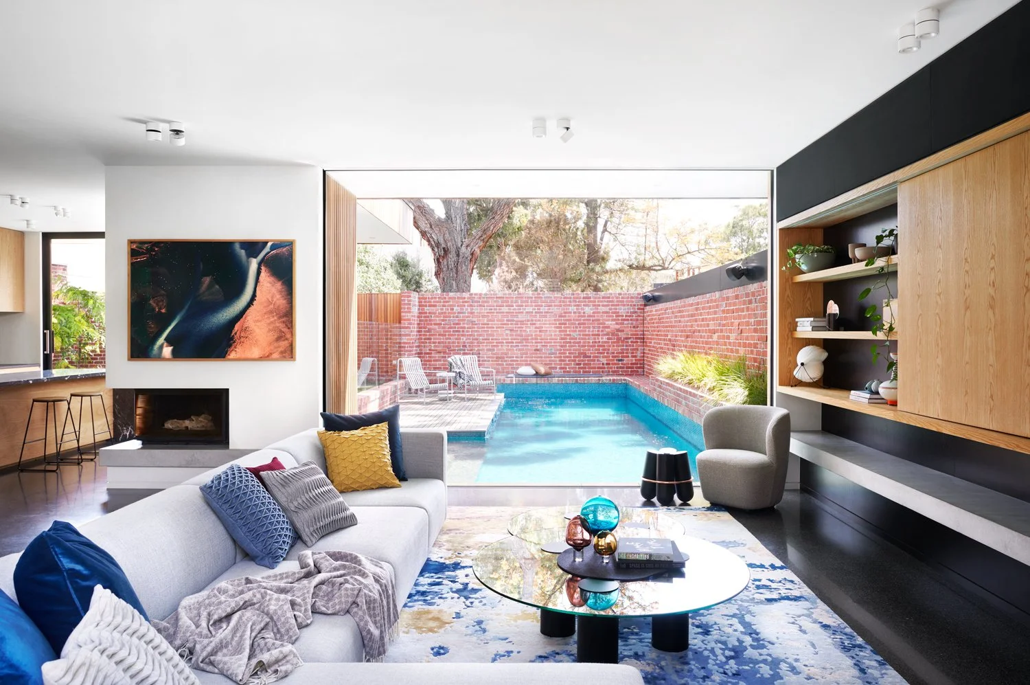 Living room with view to pool feature art over fireplace grey sofa coloured rug
