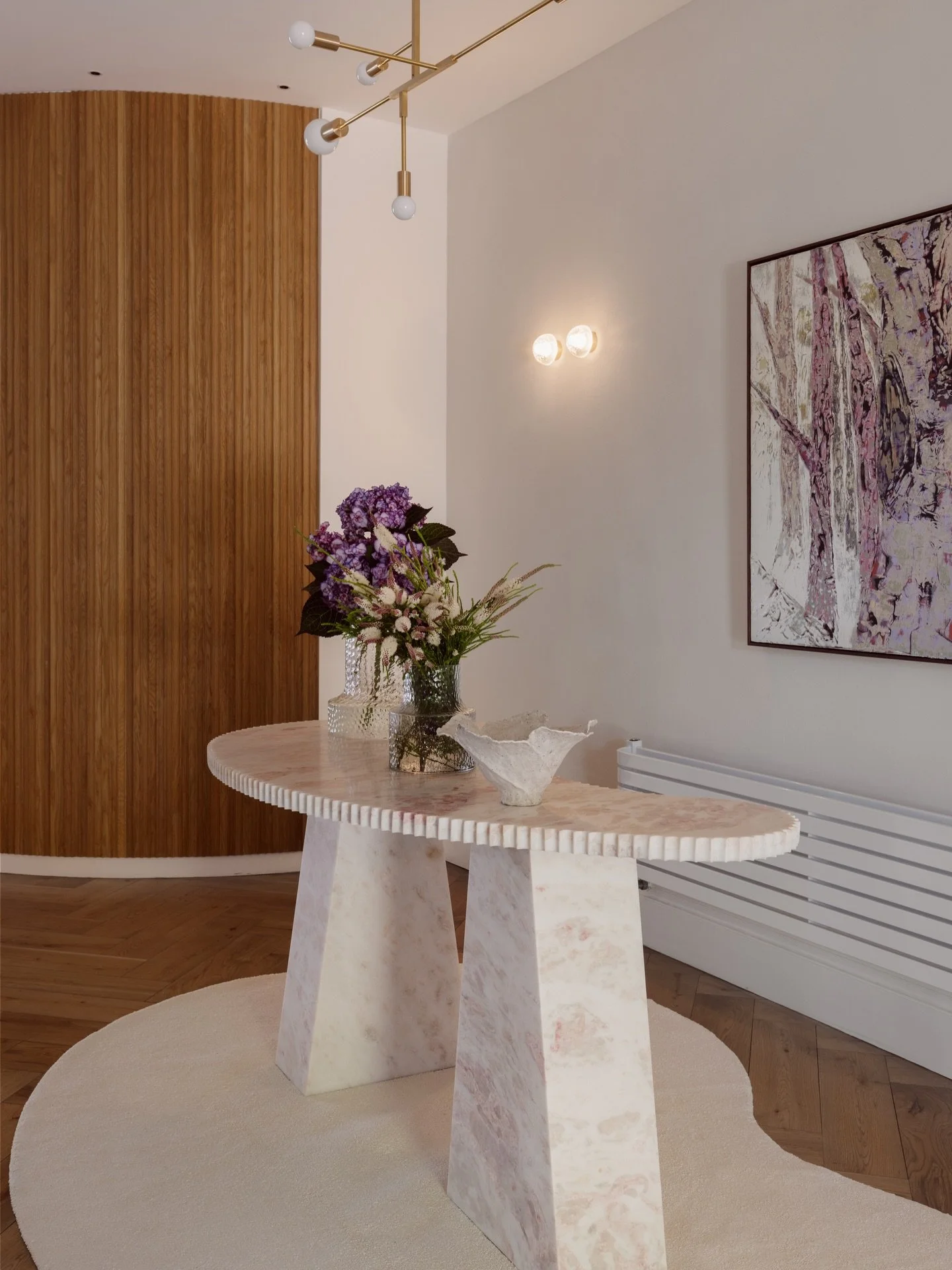 A custom sculpted console in Pink Rhino marble anchors the entry hall at Tudorlea. 

Tuscan-rendered walls, newly revived, create a soft, textural backdrop, while a glimpse of a curved batten wall subtly conceals a private lift with access to each fl