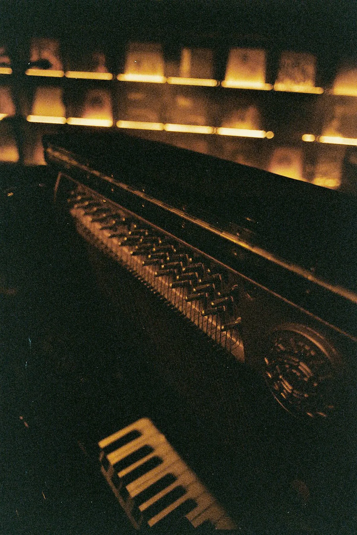 Close-up of a black grand piano with a warm glowing light in the background, illuminating the piano's interior.