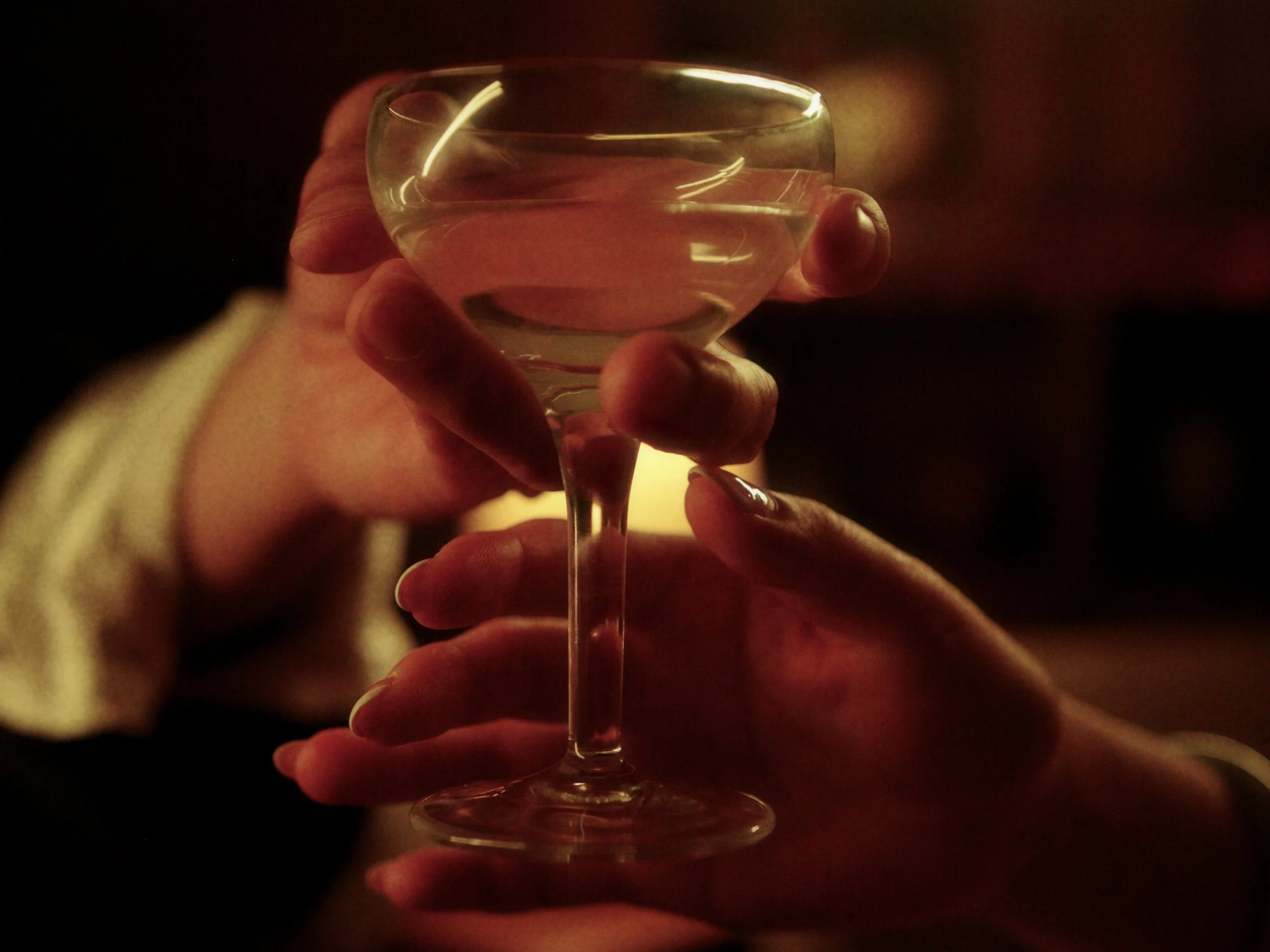 Person holding a wine glass filled with water in a dimly lit setting.