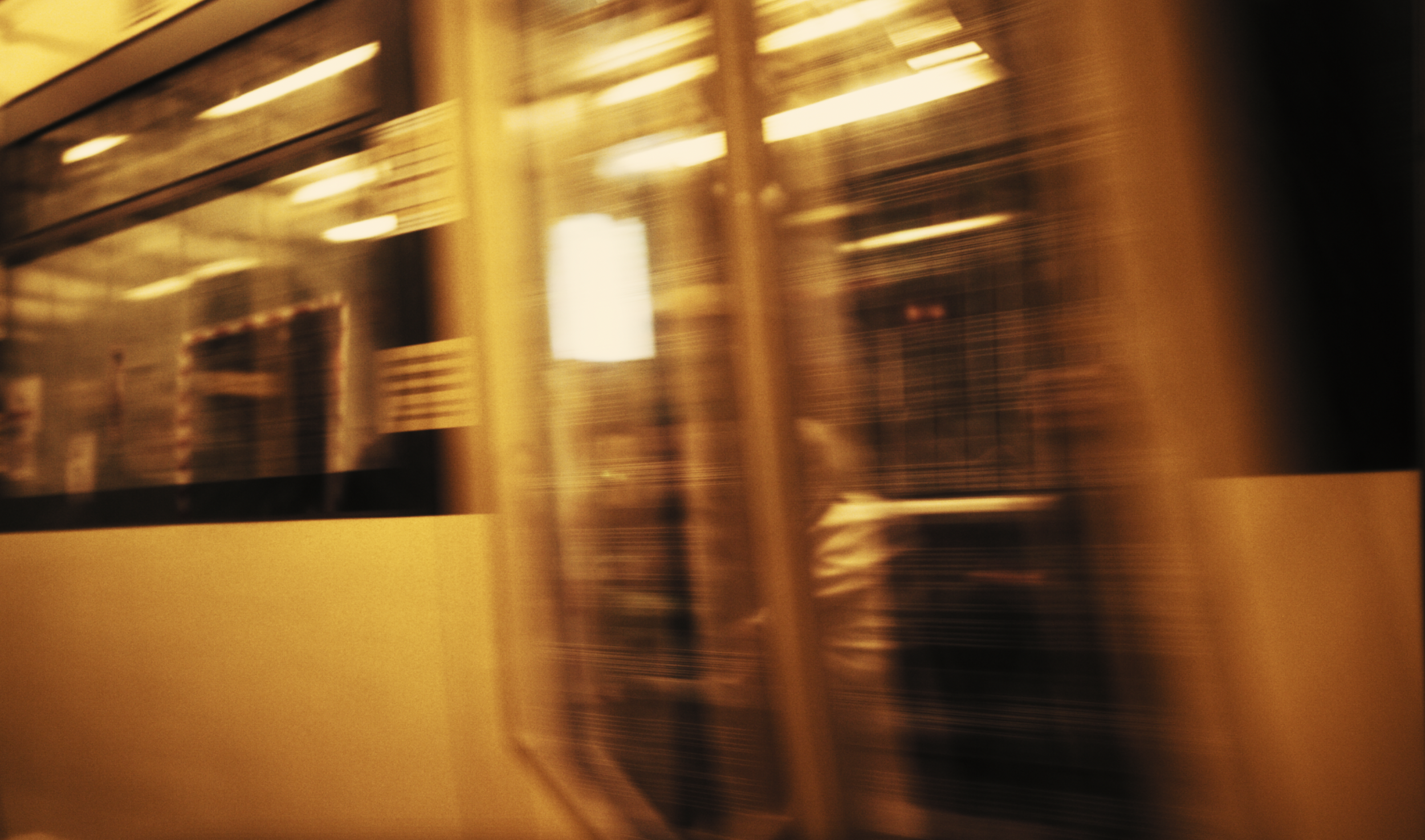 Blurred view of a corridor with reflective surfaces and warm lighting, possibly in a subway or train station.